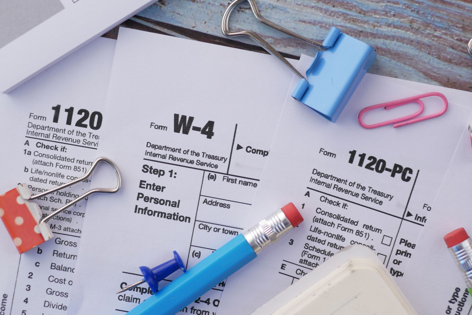 Tax forms and office supplies, including a W-4, pencils, paper clips, and binder clips.