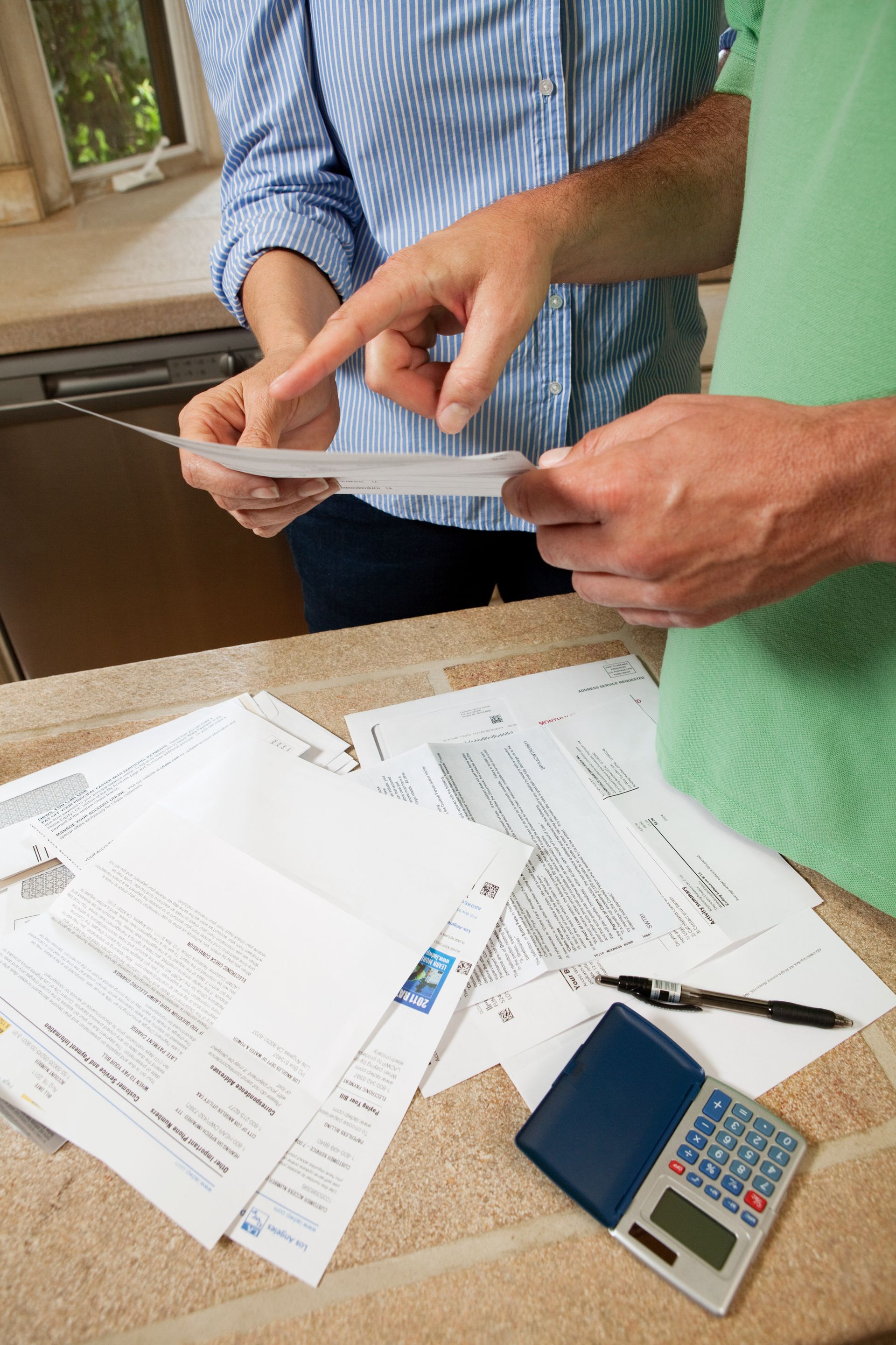 People reviewing bills on a countertop, pointing, with a calculator and pen.