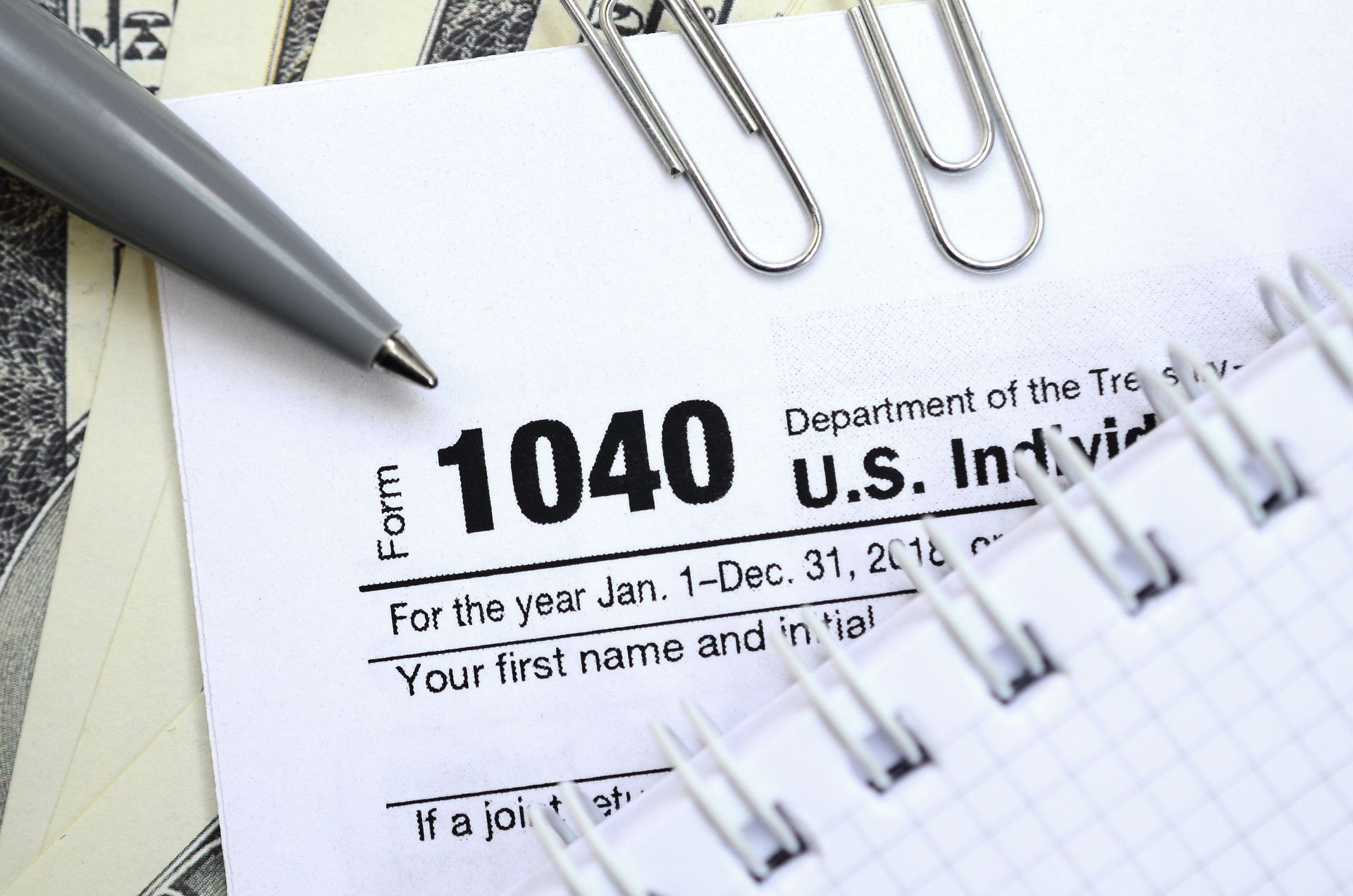 Form 1040 tax form with pen, paper clips, and money, preparing taxes.