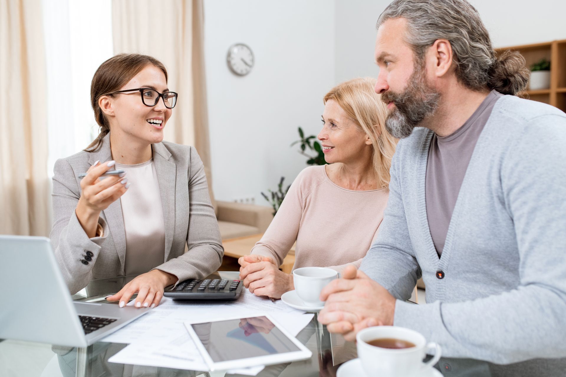 Financial advisor talking with a couple; laptop, calculator, and coffee on table.