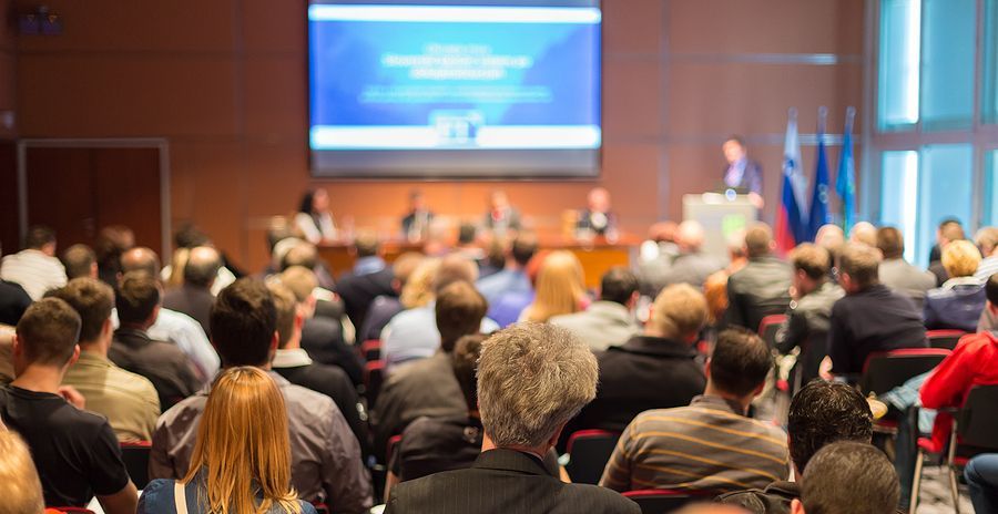 A large group of people are sitting in a conference room watching a presentation.