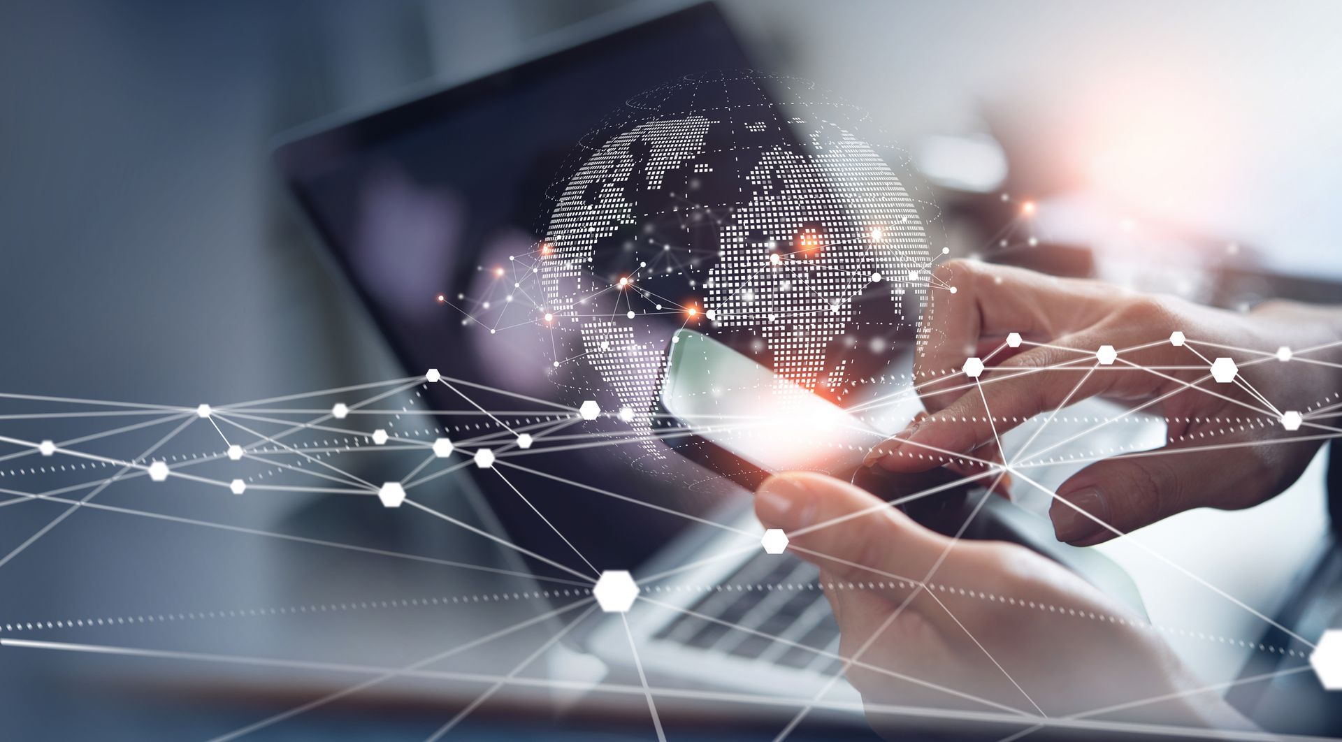 Una persona tiene in mano un telefono cellulare davanti a un computer portatile.