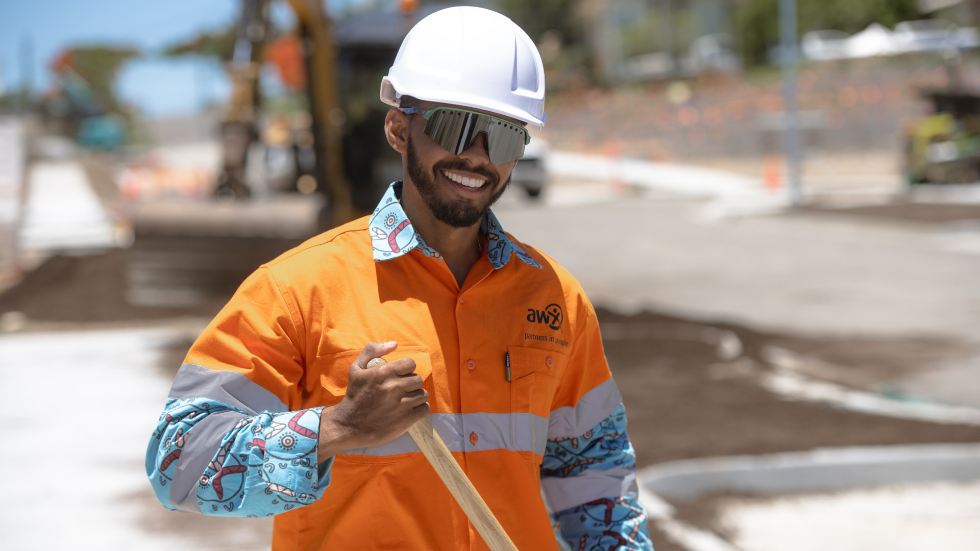 Three people in orange workwear on a construction site. One holds a shovel.