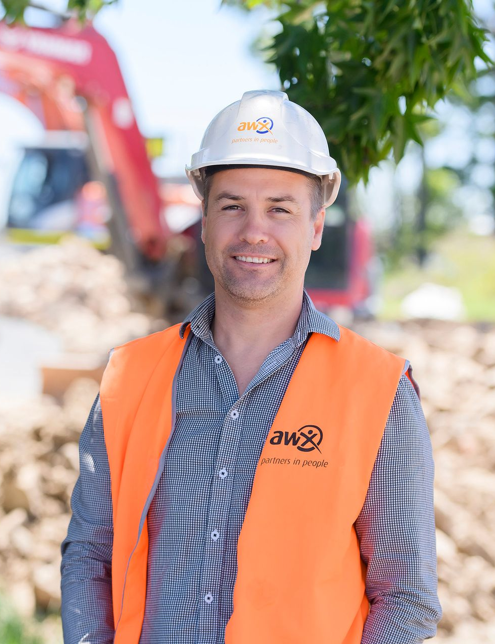 Man in hard hat and safety vest smiles at the camera on a construction site.