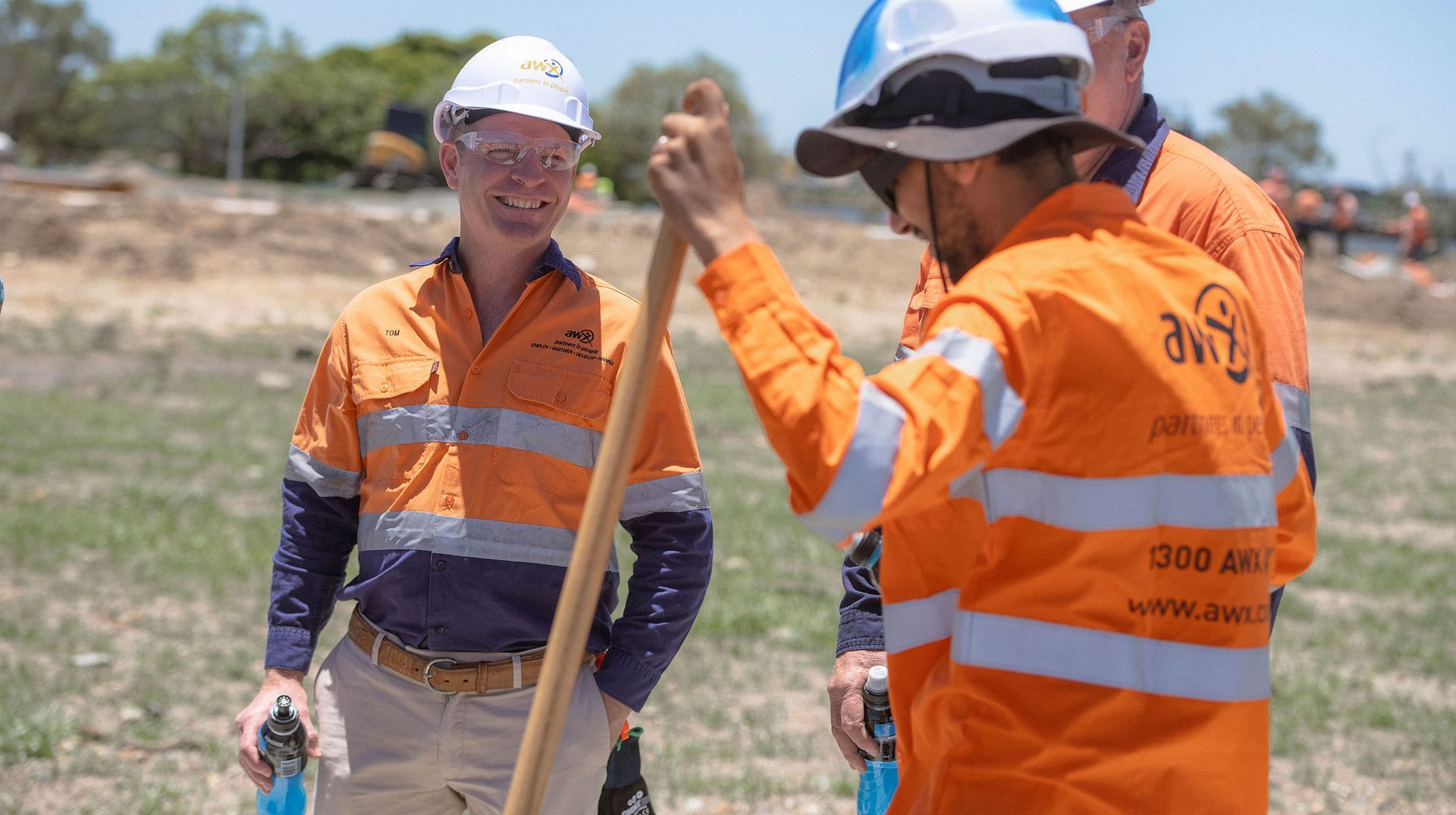 Construction workers in orange safety gear and hard hats on site.