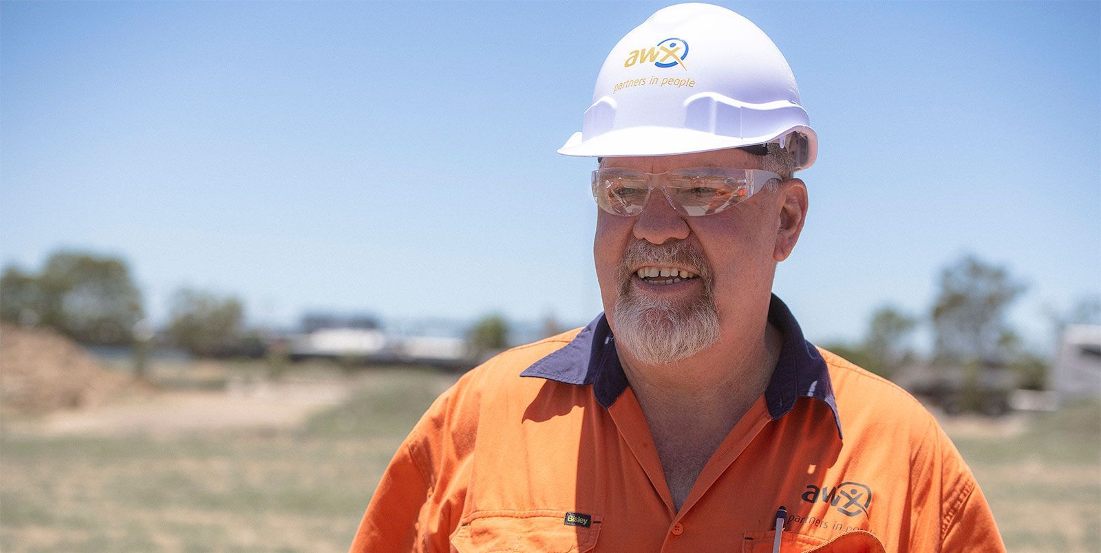 Man wearing hard hat and orange work shirt smiles outside on a sunny day.