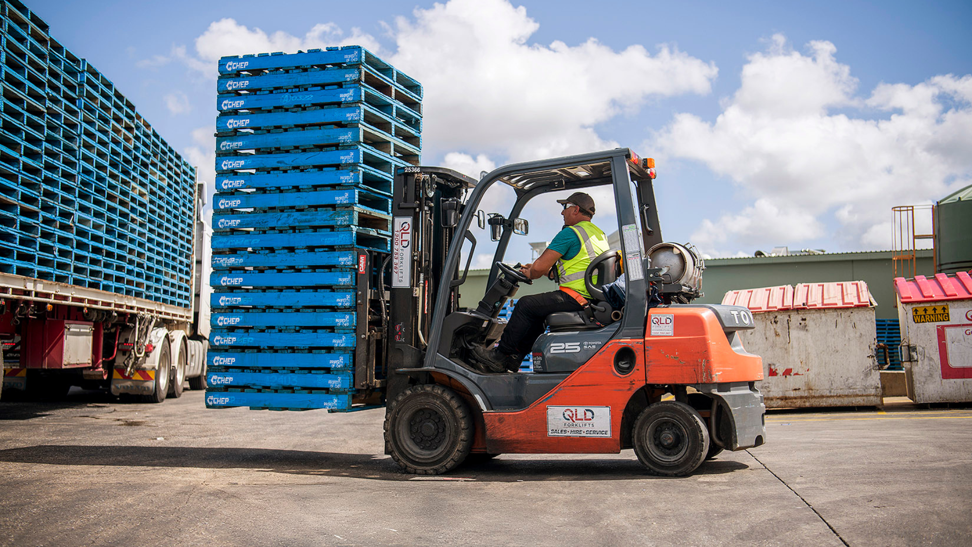 Man in orange workwear and hard hat smiles outdoors.