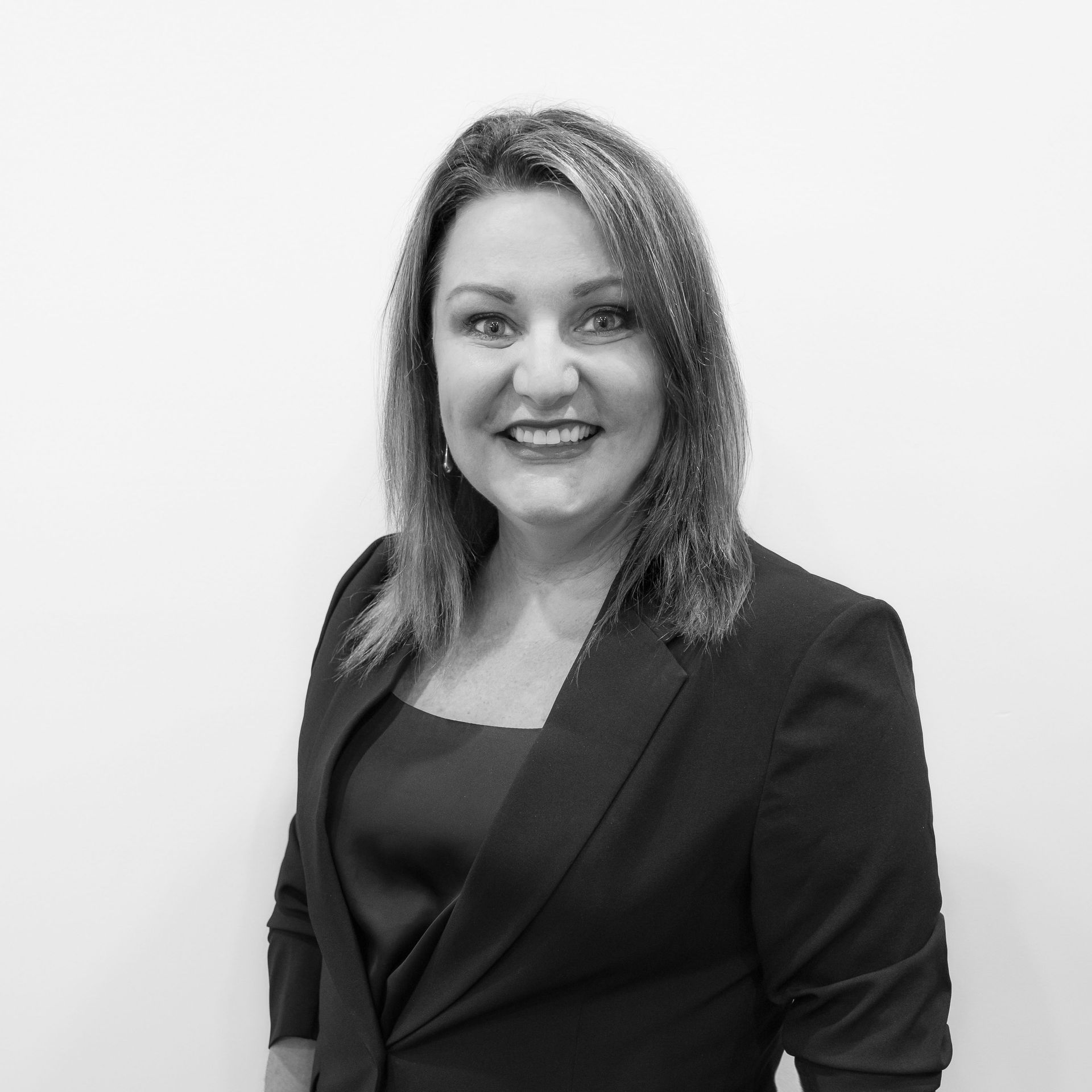 Man in construction workwear, arms crossed, smiling. Hard hat, excavator in background.