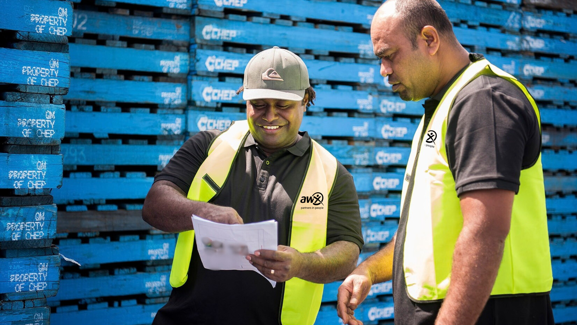 Man in orange workwear and hard hat smiles outdoors.
