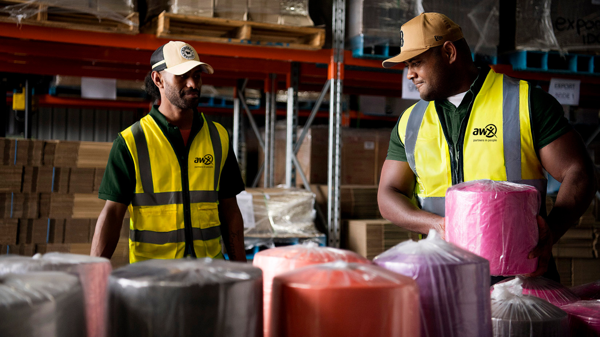 Man in orange workwear and hard hat smiles outdoors.