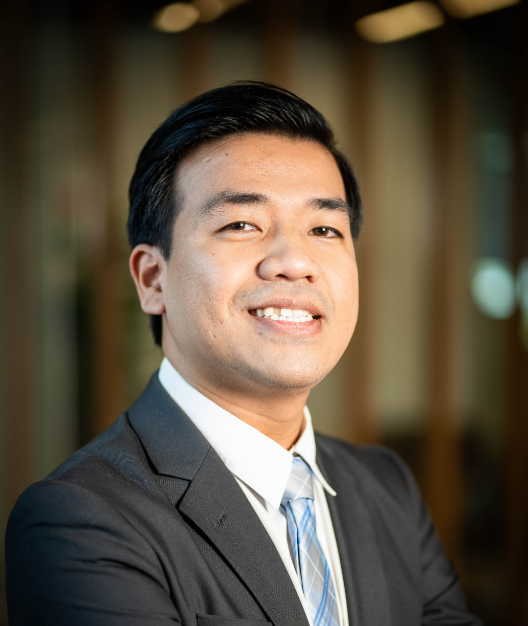 Man in construction workwear, arms crossed, smiling. Hard hat, excavator in background.