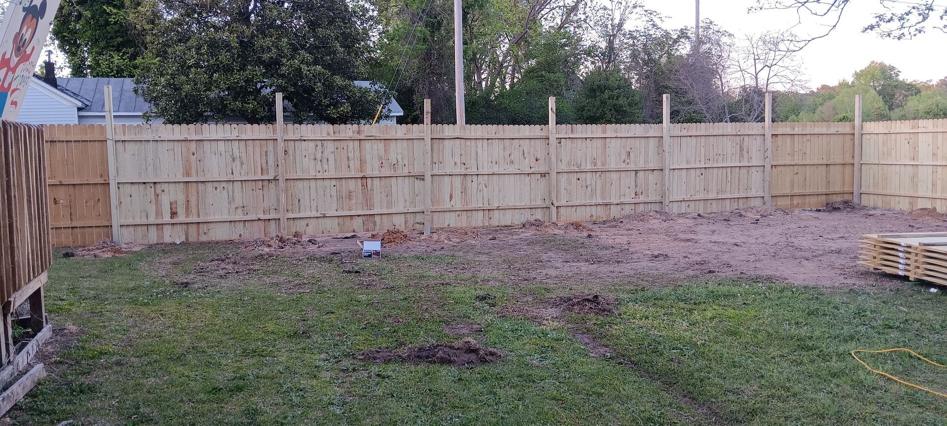 A wooden fence is being built in the backyard of a house.