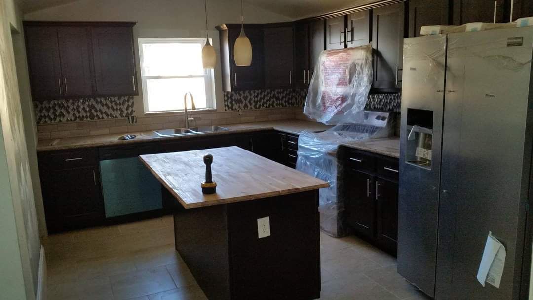 A kitchen with a large island in the middle and a stainless steel refrigerator.