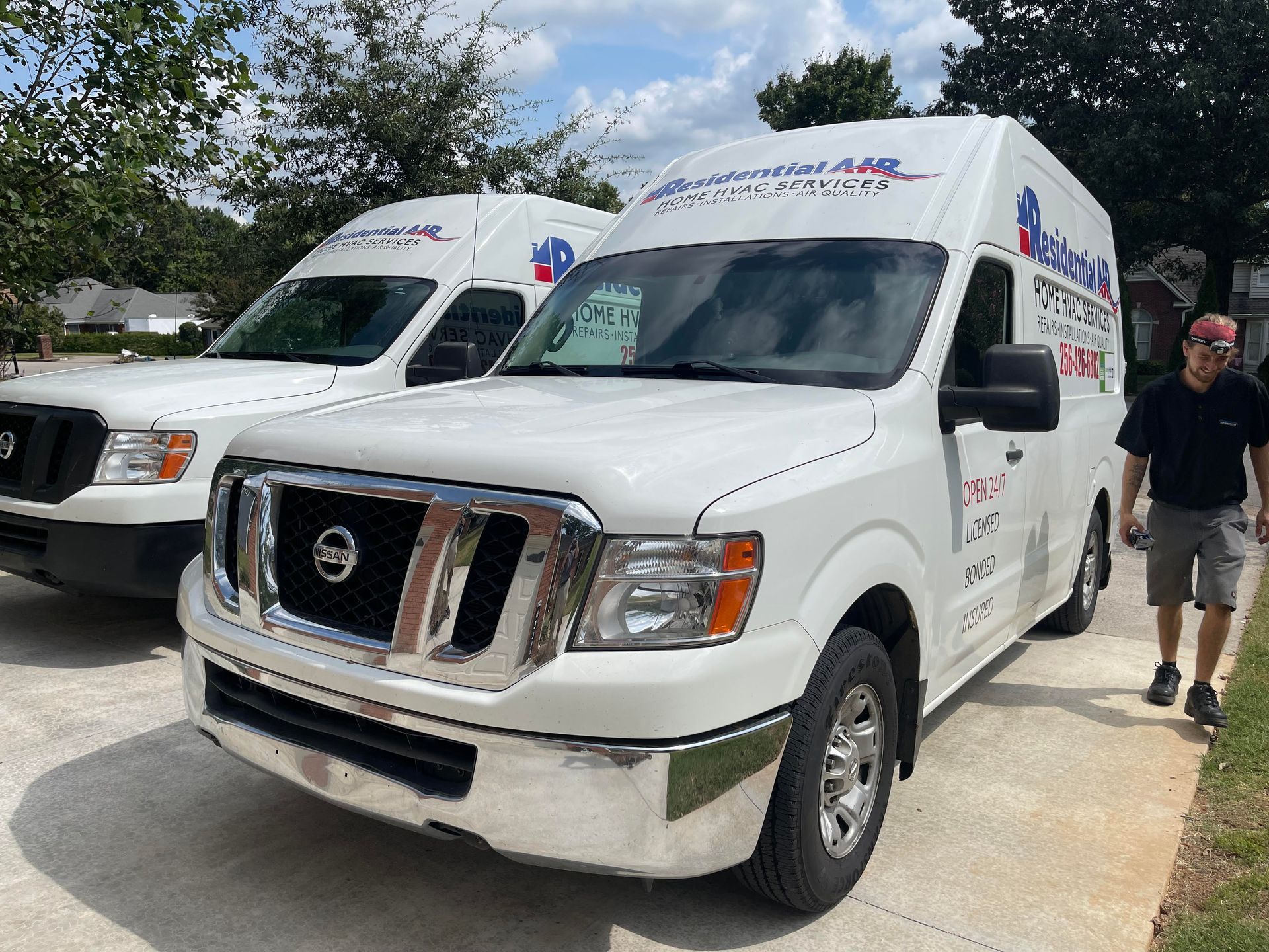 Two white vans with company logos parked on a driveway; a man walks nearby.