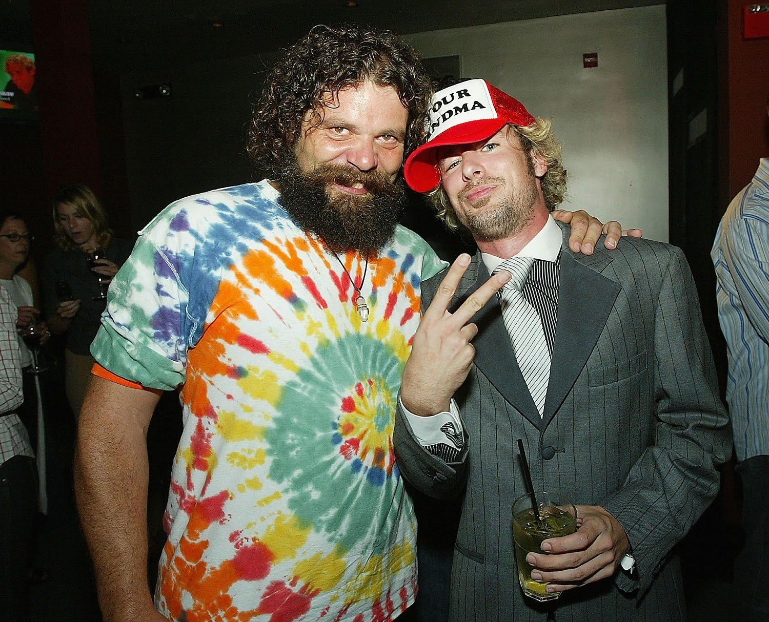 A man in a tie dye shirt and a man in a suit are posing for a picture