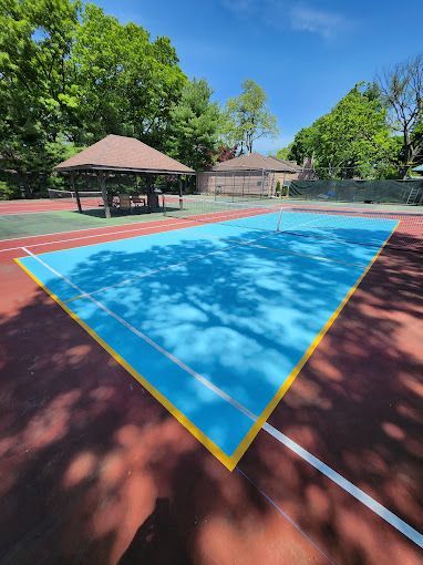 A blue and yellow tennis court with a pavilion in the background.