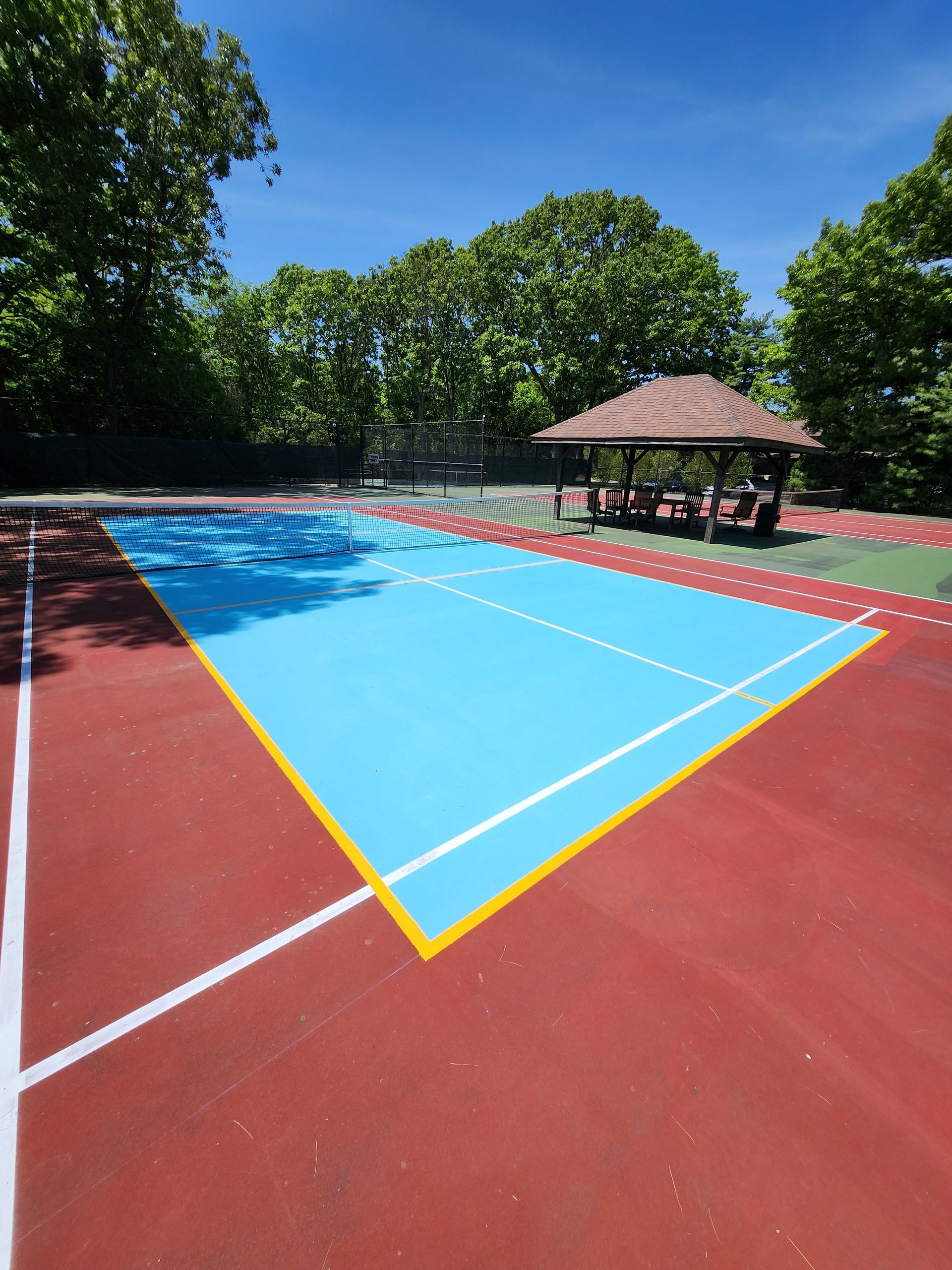 A blue and red tennis court with a gazebo in the background