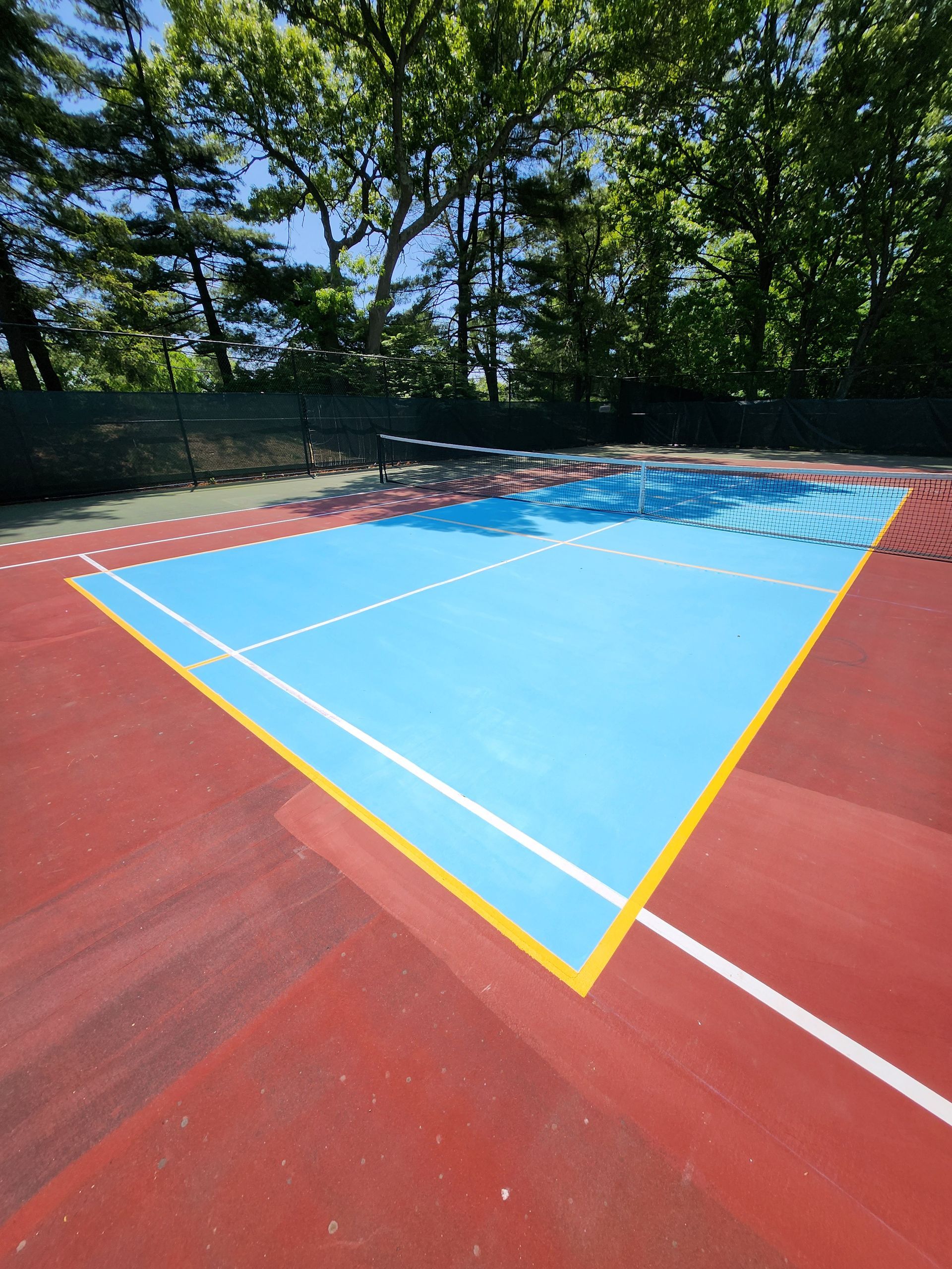 A blue and red tennis court with trees in the background