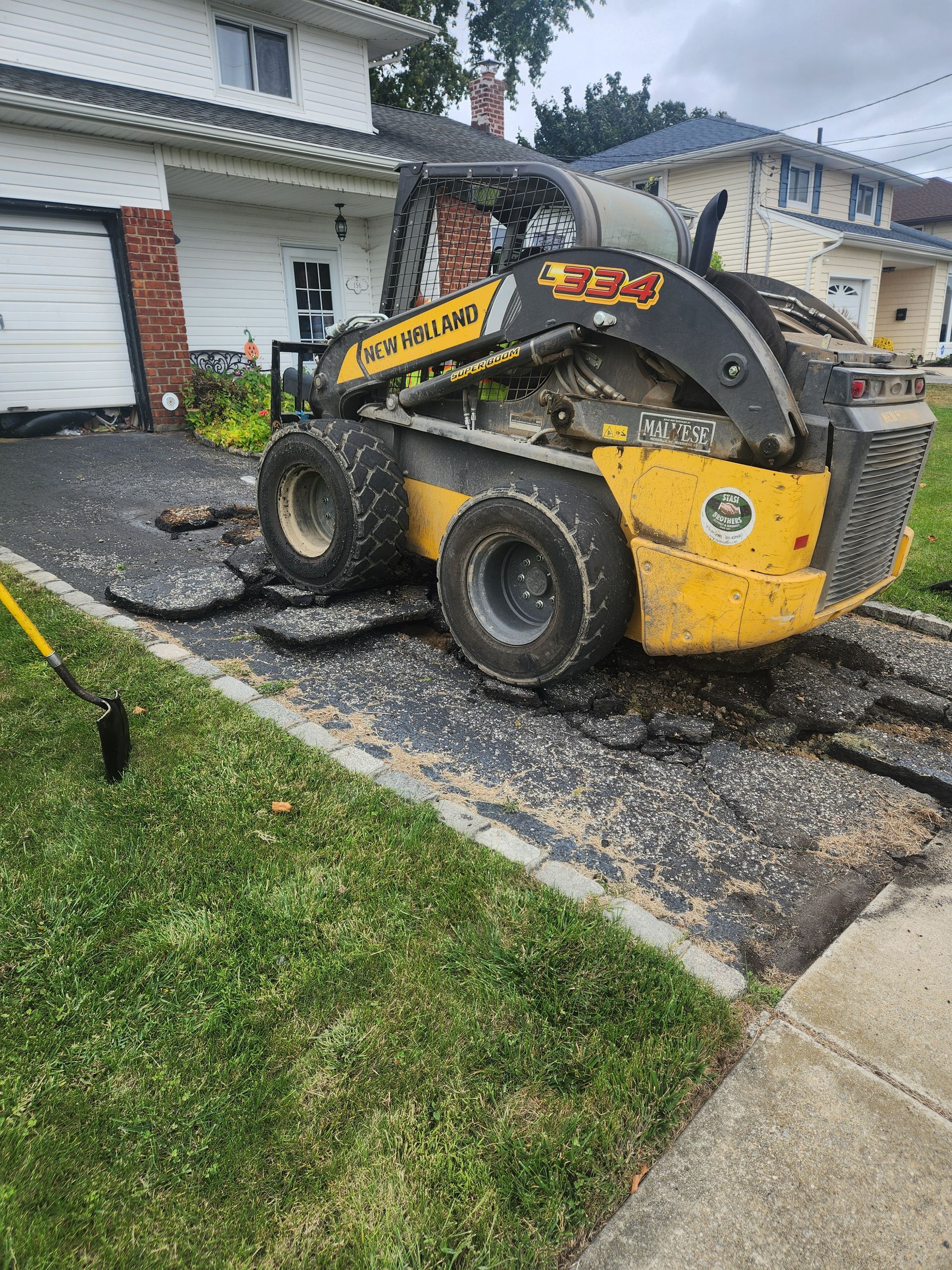 A yellow and black skid steer is parked in front of a house.