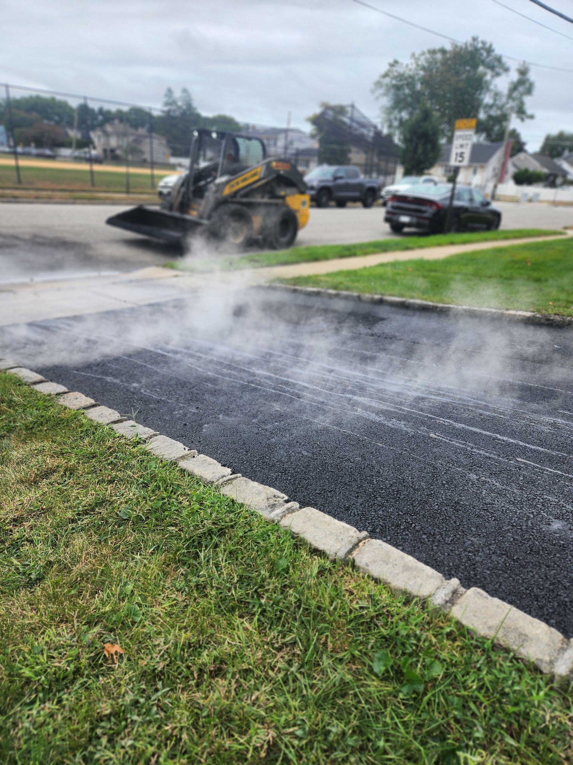 A bulldozer is spreading asphalt on the side of a road.