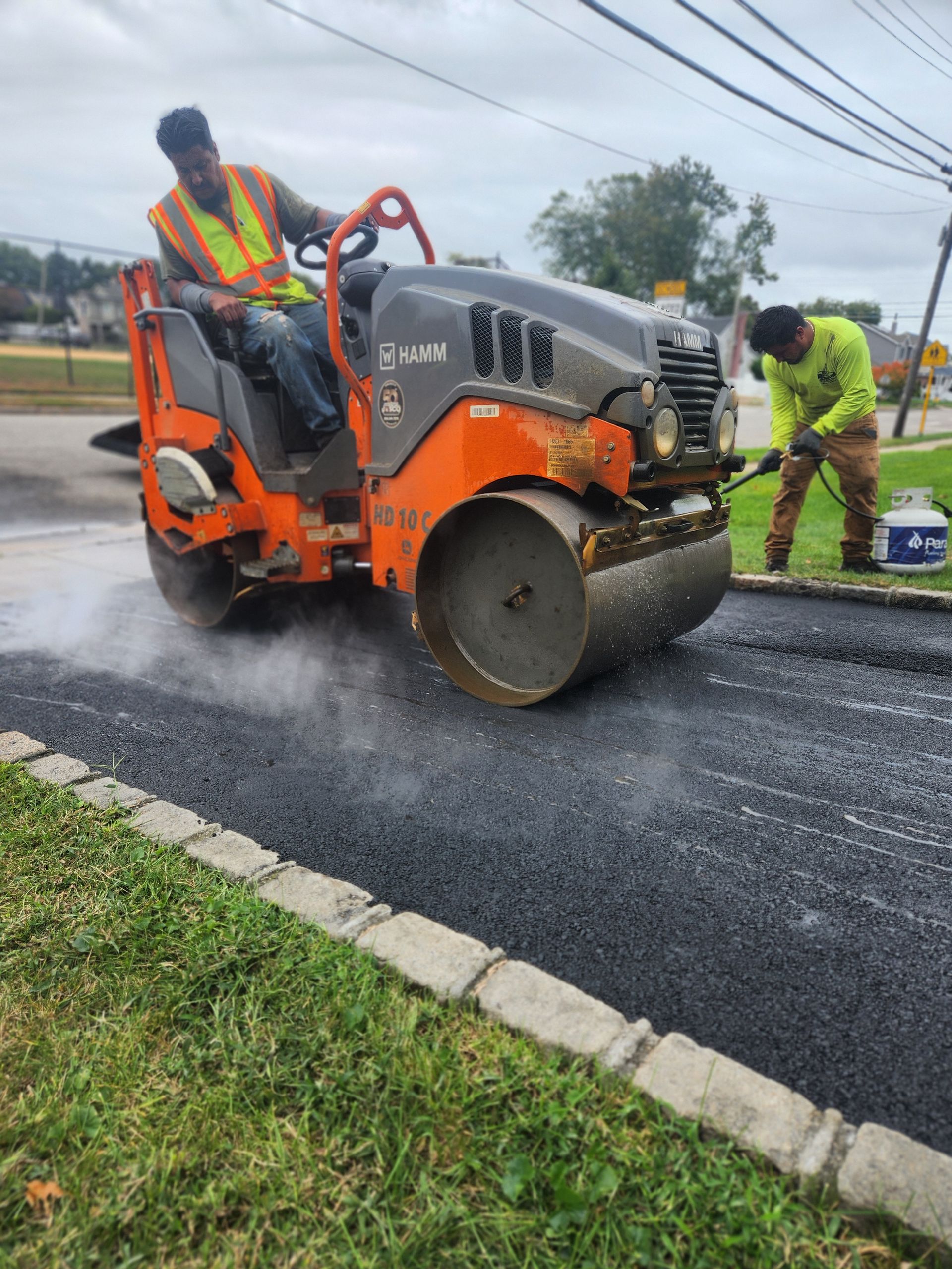 Two men are working on a road with a roller.