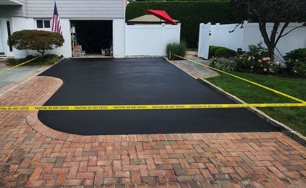 A man is painting a driveway with a broom.