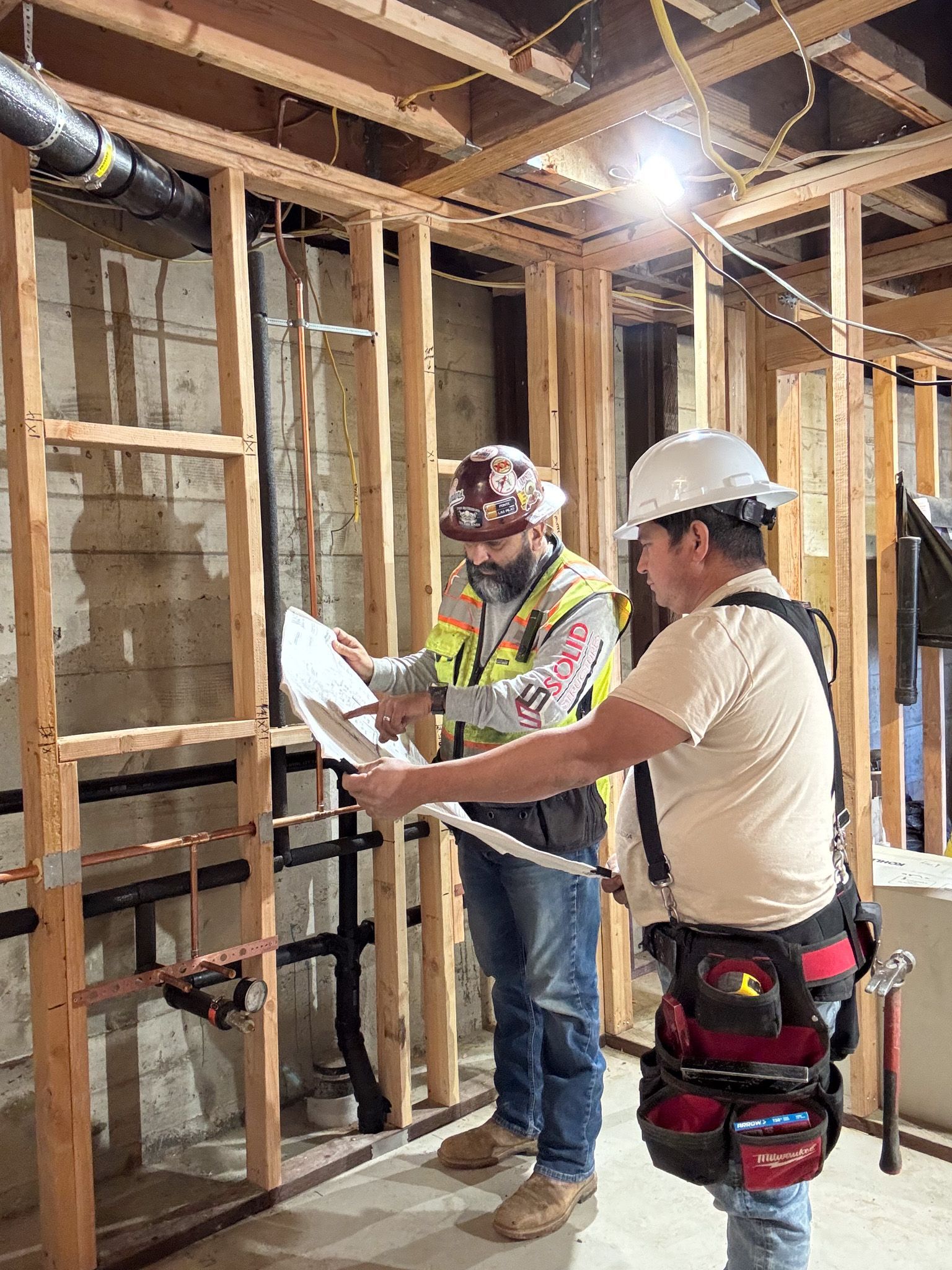 Construction workers building a wooden frame. They wear helmets, use tools, and work outdoors on a sunny day.