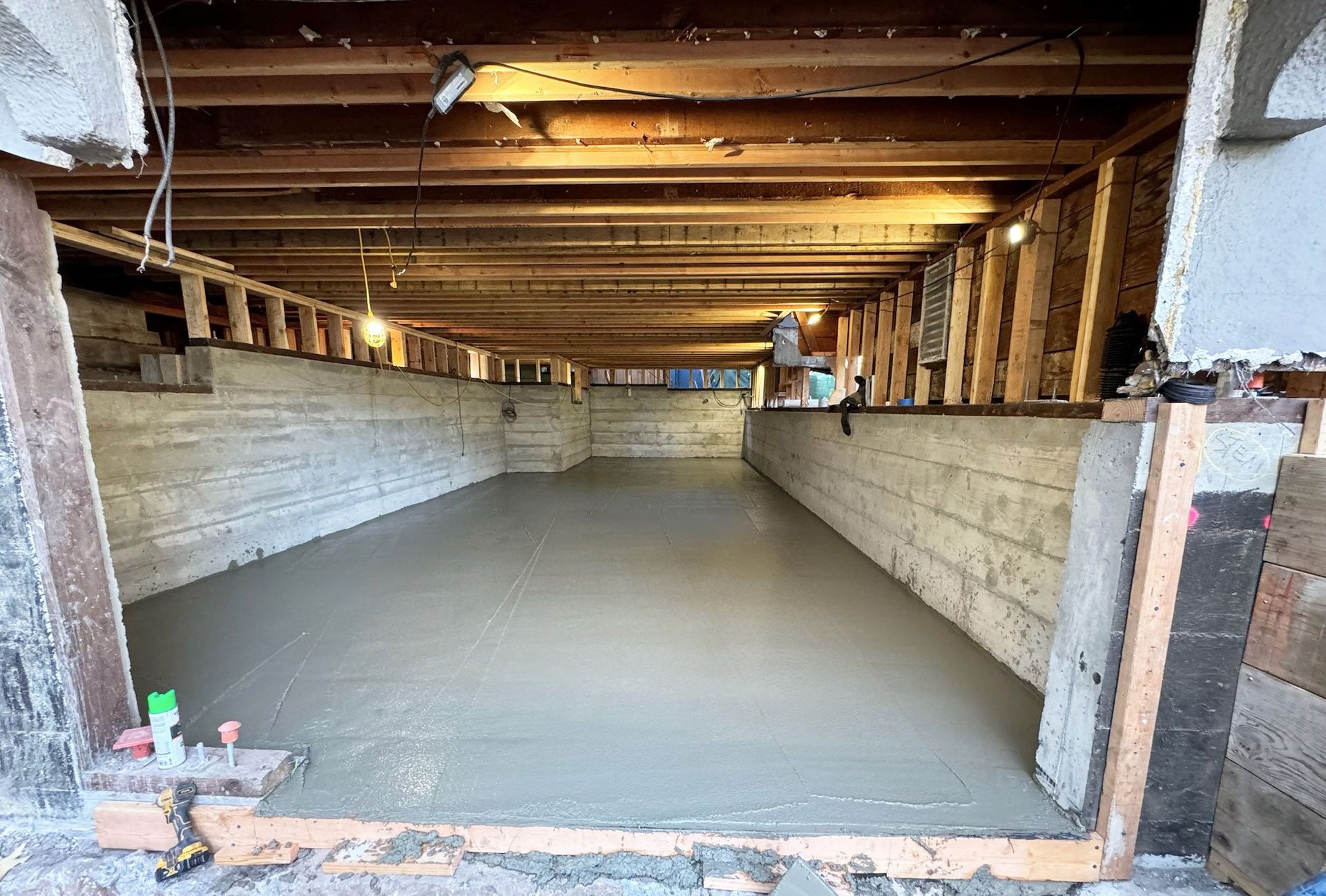 Construction workers pouring and leveling wet concrete into a wooden frame at a building site.