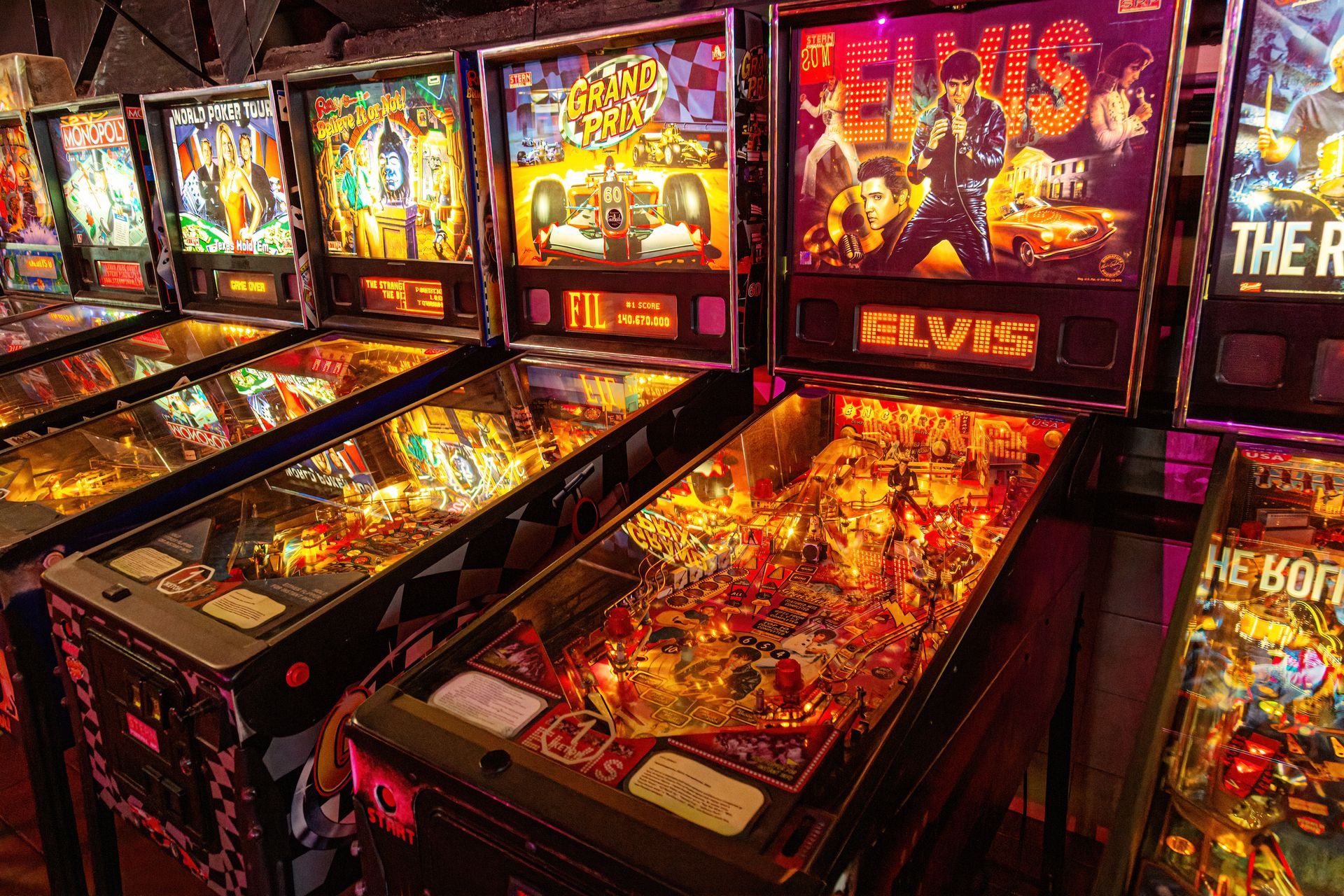 Row of illuminated pinball machines, including an Elvis-themed one.