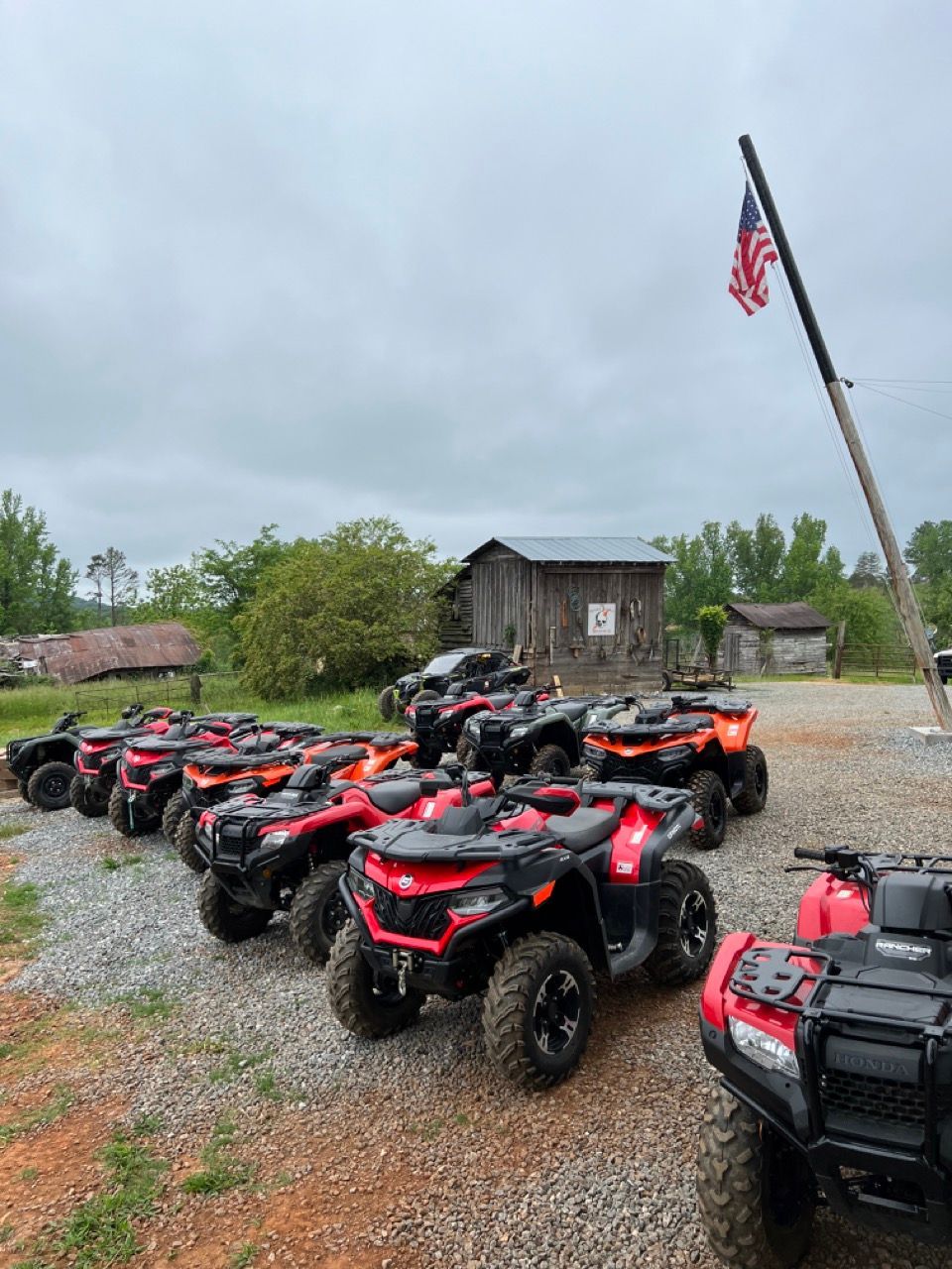 ATVs parked in a gravel lot next to a small wooden building with an American flag on a pole.