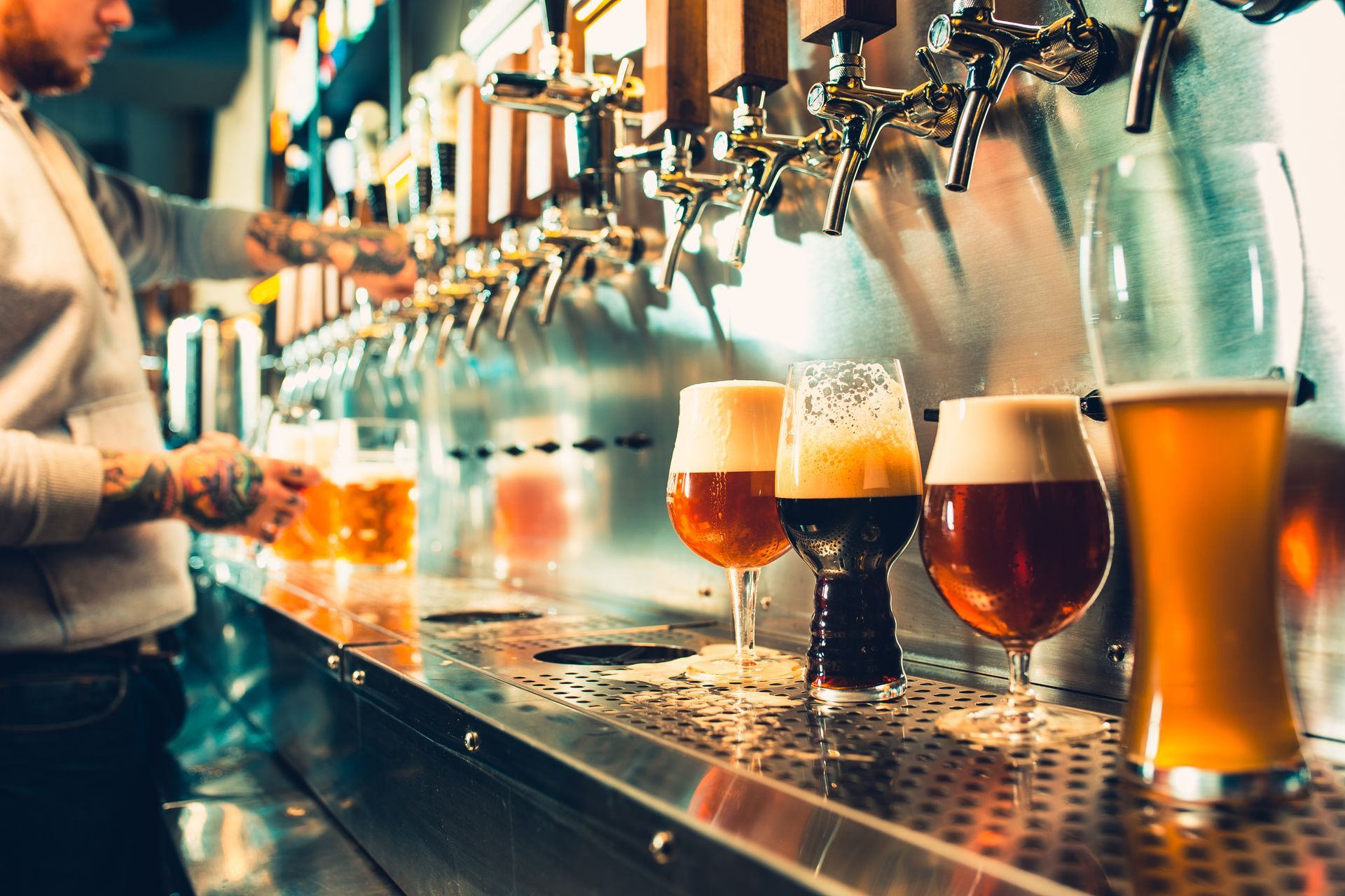 A bartender pouring beer at a tap. Several beer glasses with different colored brews sit on the bar.