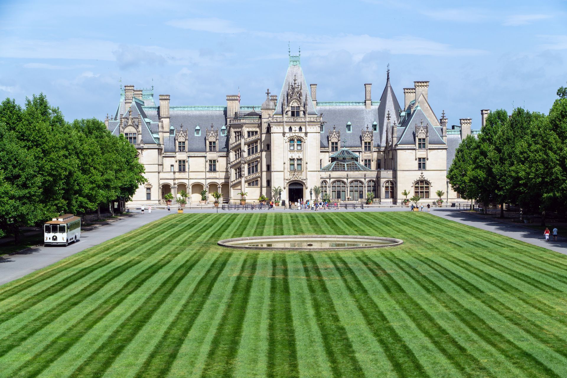 Biltmore Estate with striped green lawn. Cream-colored mansion in background, clear blue sky overhead.