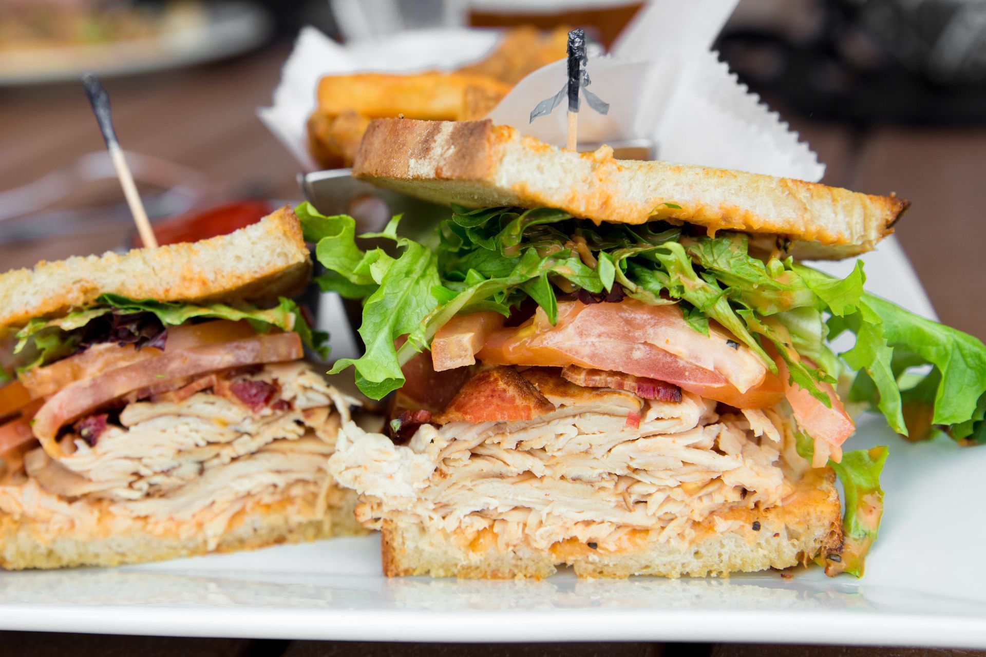 Turkey club sandwich with bacon, lettuce, and tomato on toasted bread, cut in half.