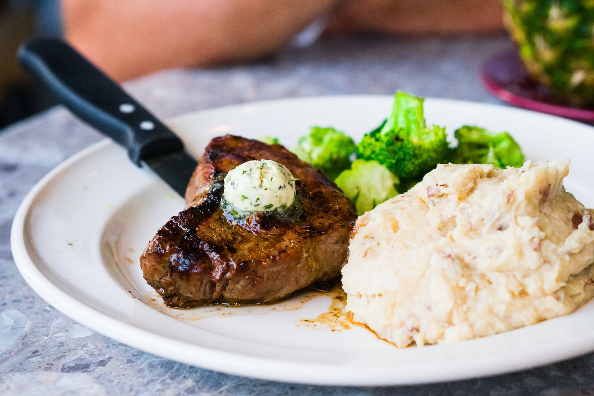 Steak with butter, mashed potatoes, and broccoli on a white plate with a knife.