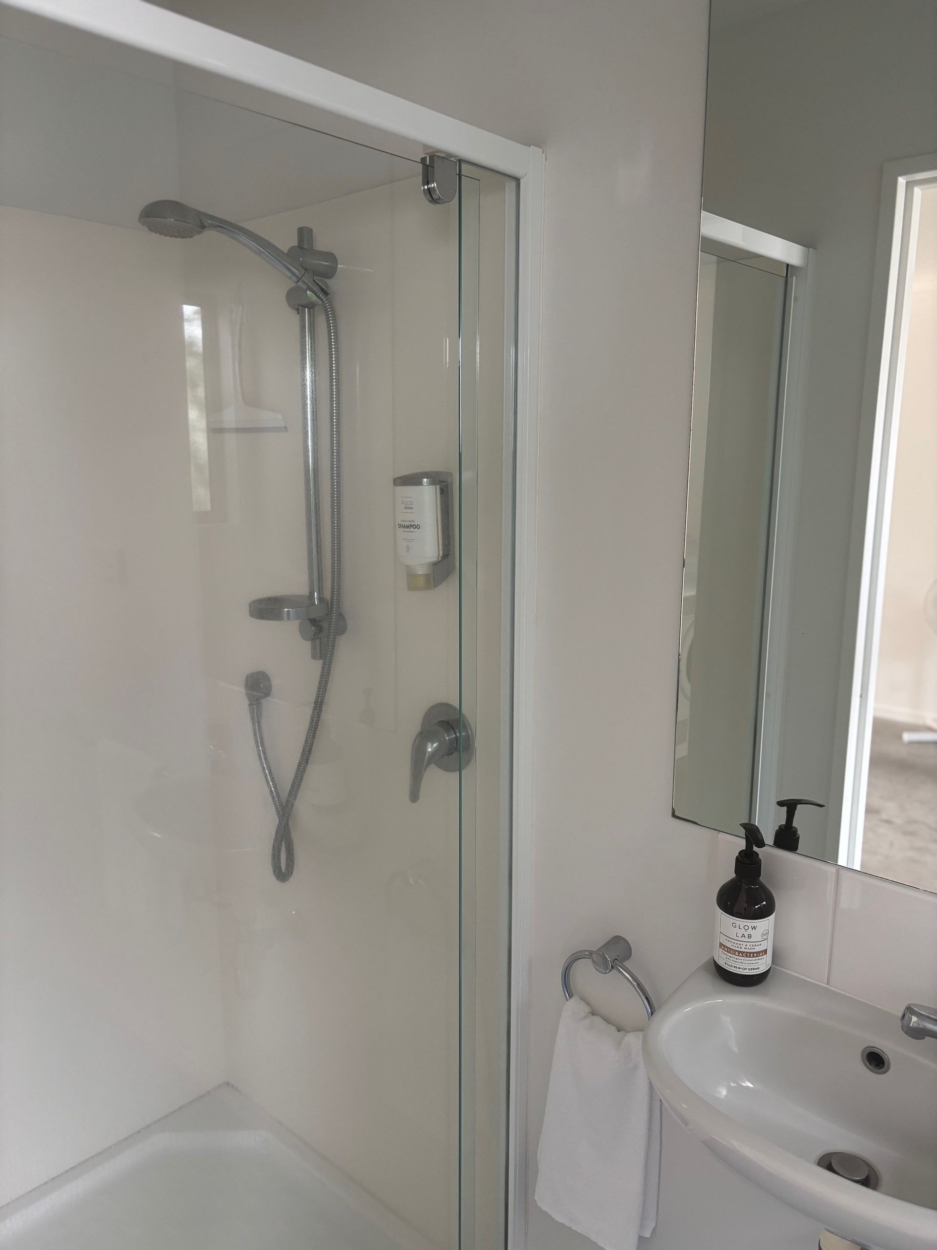 Small bathroom with a walk-in shower, sink, mirror, and towel rack.