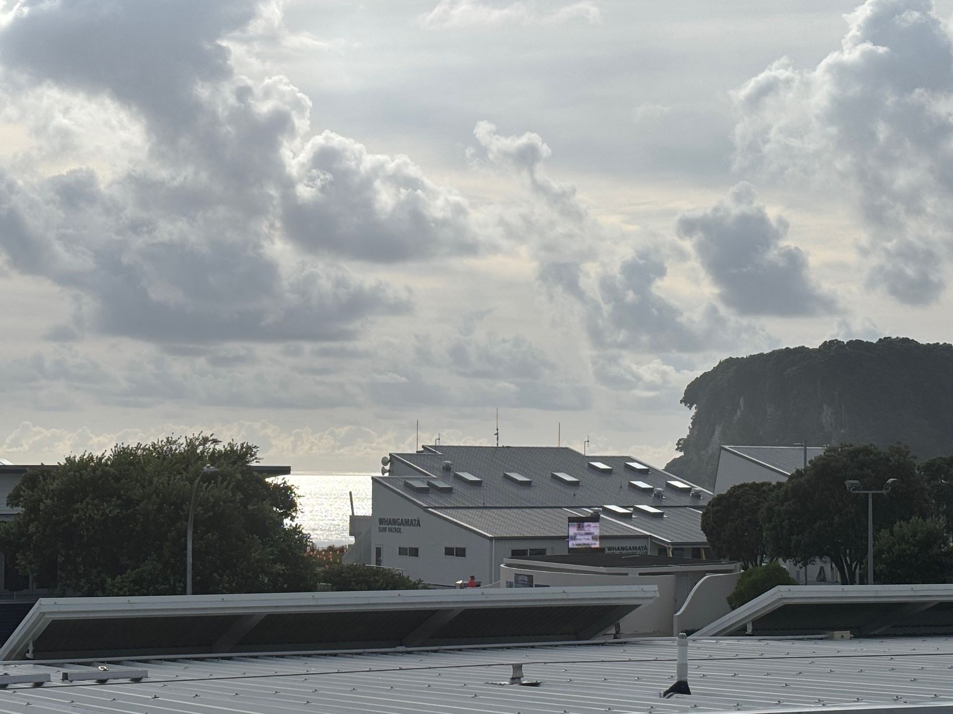 Cloudy sky over a harbor with buildings, boats, and a forested hill in the distance