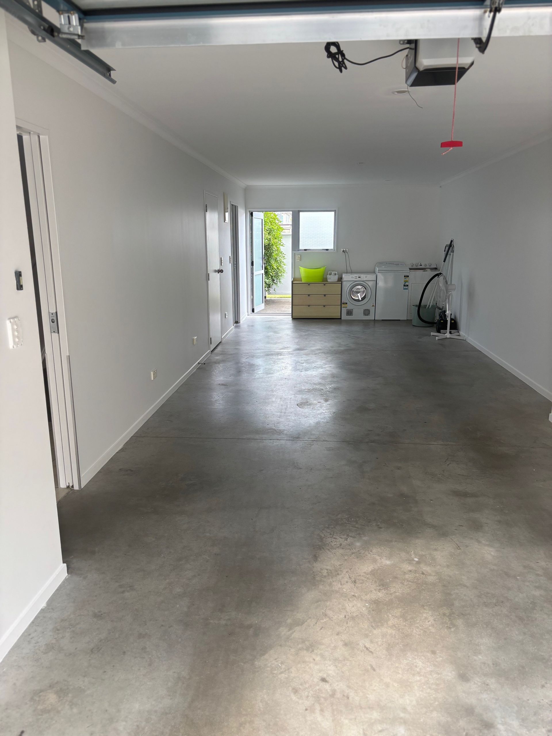 Empty garage interior with concrete floor, white walls, and open door to a bright outdoor area
