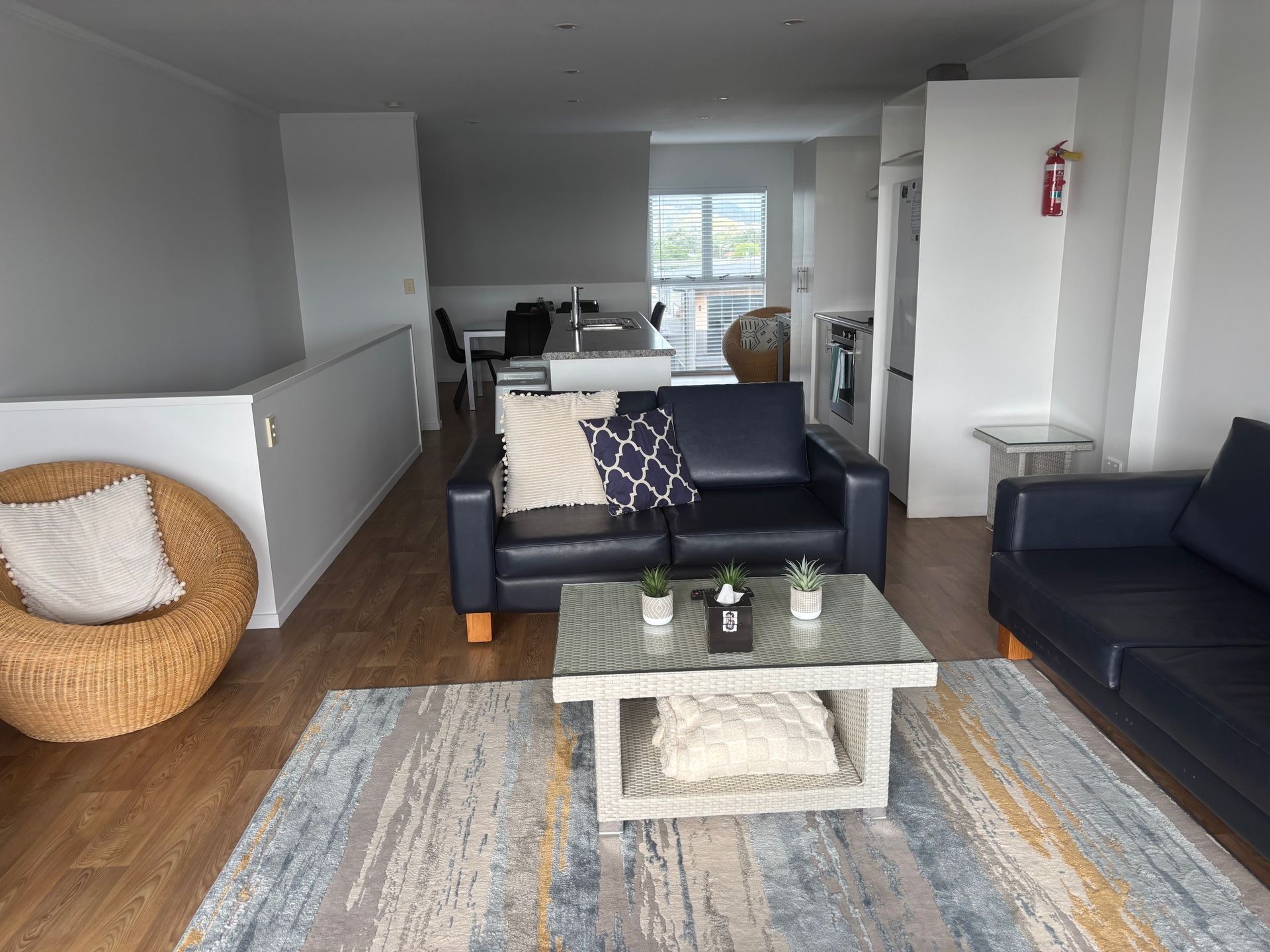 Living room with navy sofas, a glass coffee table, and a wicker chair in a modern open-plan apartment