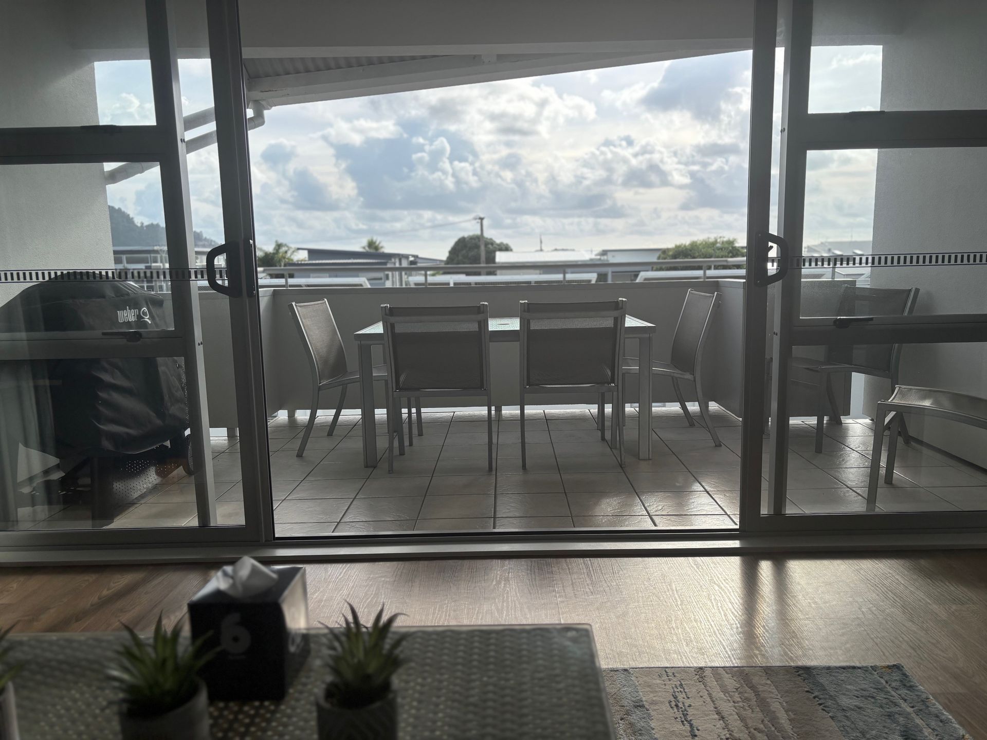 Modern patio balcony with table, chairs, glass doors, and ocean view at sunset