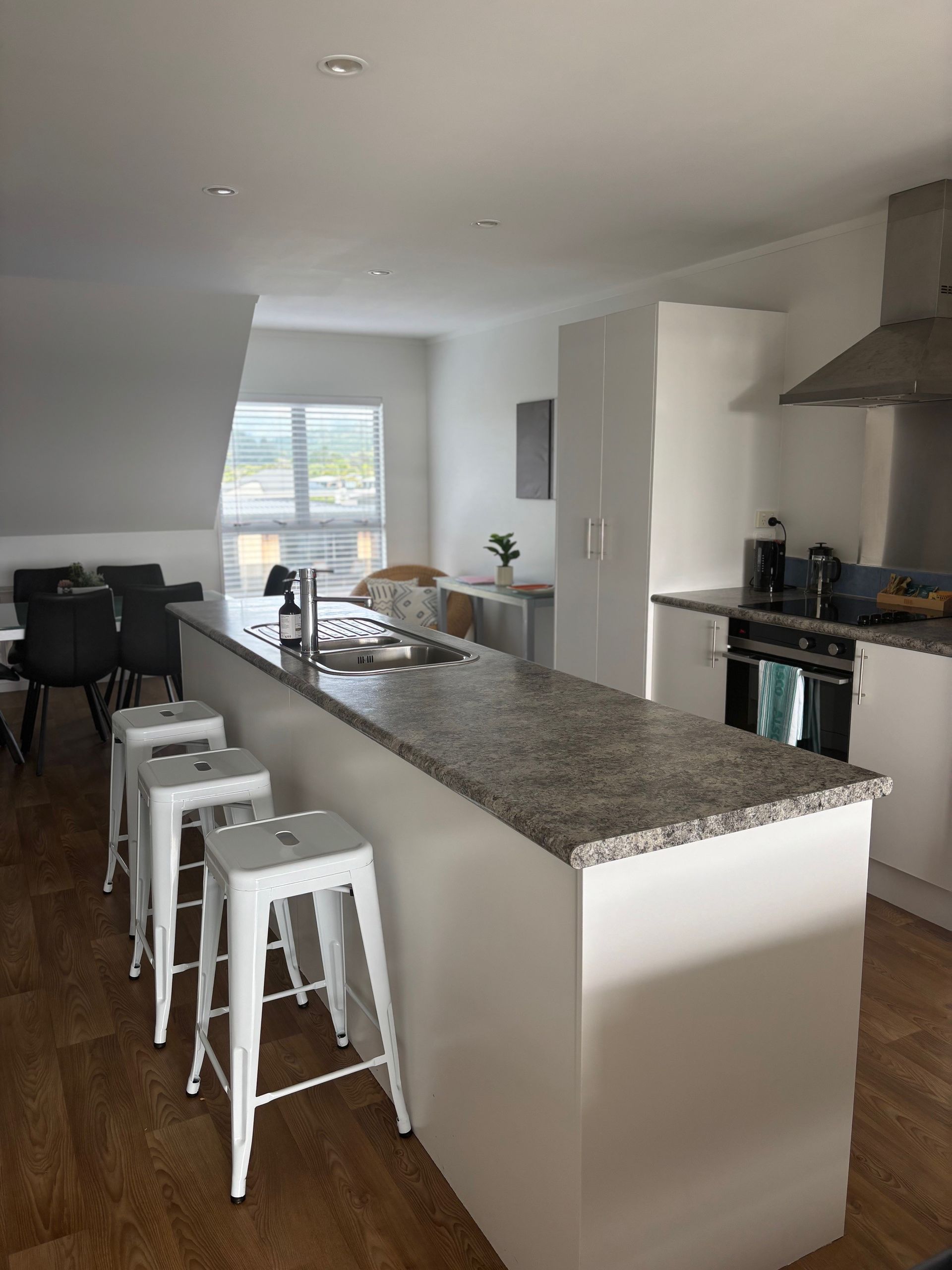 Modern kitchen with granite island, white stools, and dining area by a window