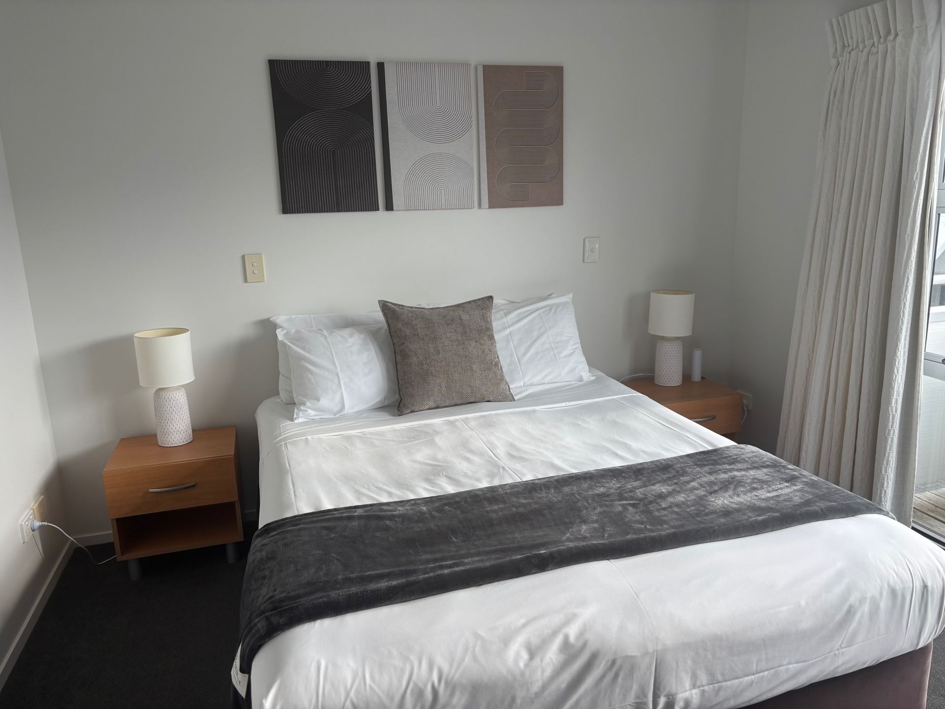 Neatly made bedroom with a white bed, gray throw, matching lamps, and artwork above the headboard