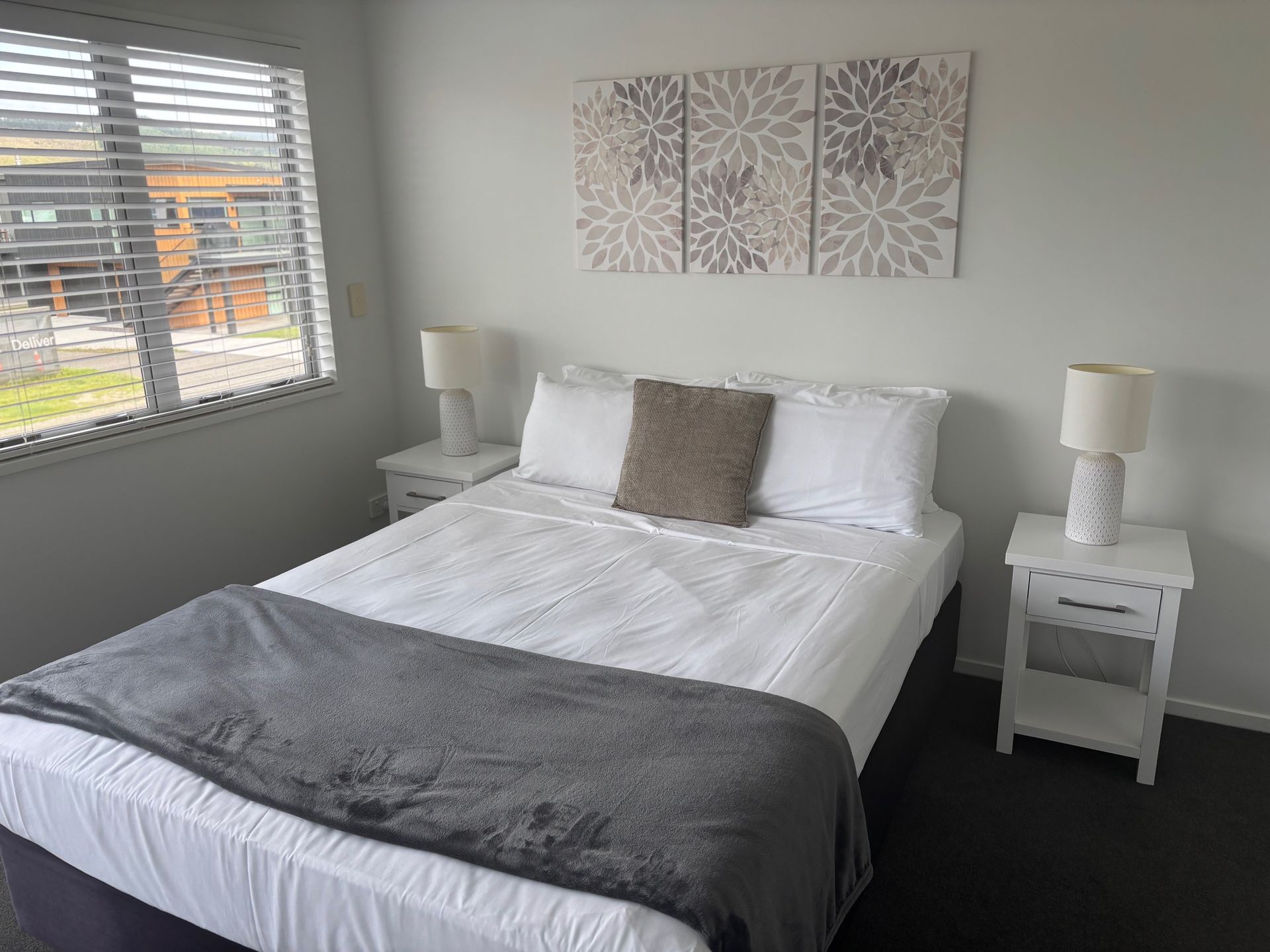 Bright bedroom with a white bed, gray blanket, matching nightstands, and wall art near a window.