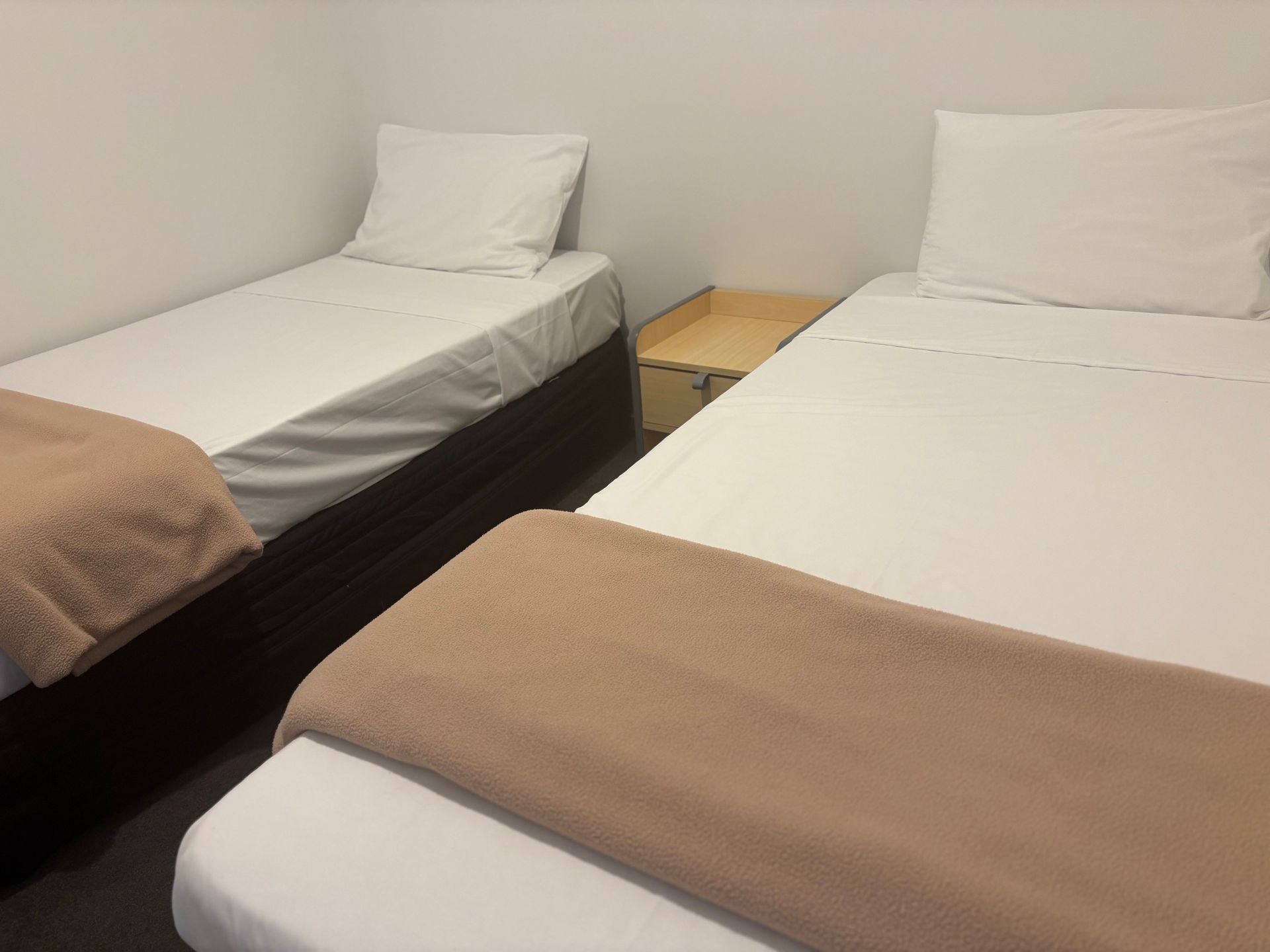 Two single beds with white linens and beige blankets in a simple bedroom