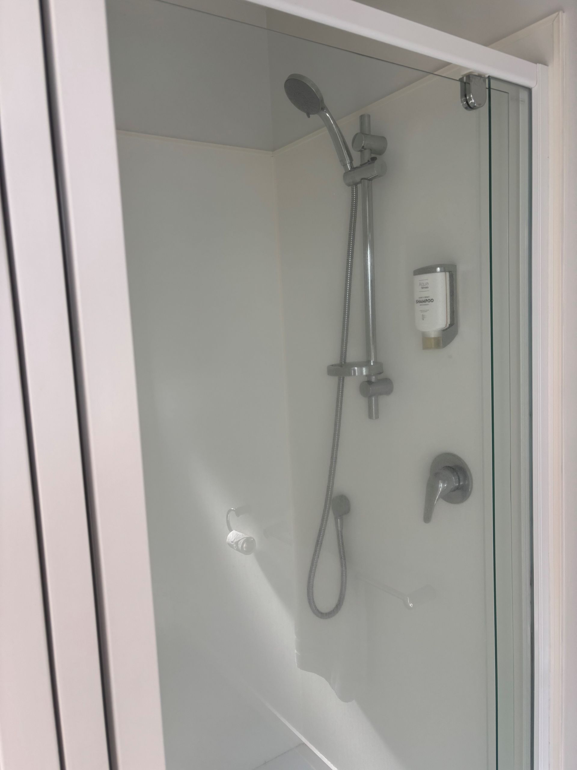 A white shower stall featuring a chrome adjustable showerhead, a wall-mounted soap dispenser, and a single lever faucet.