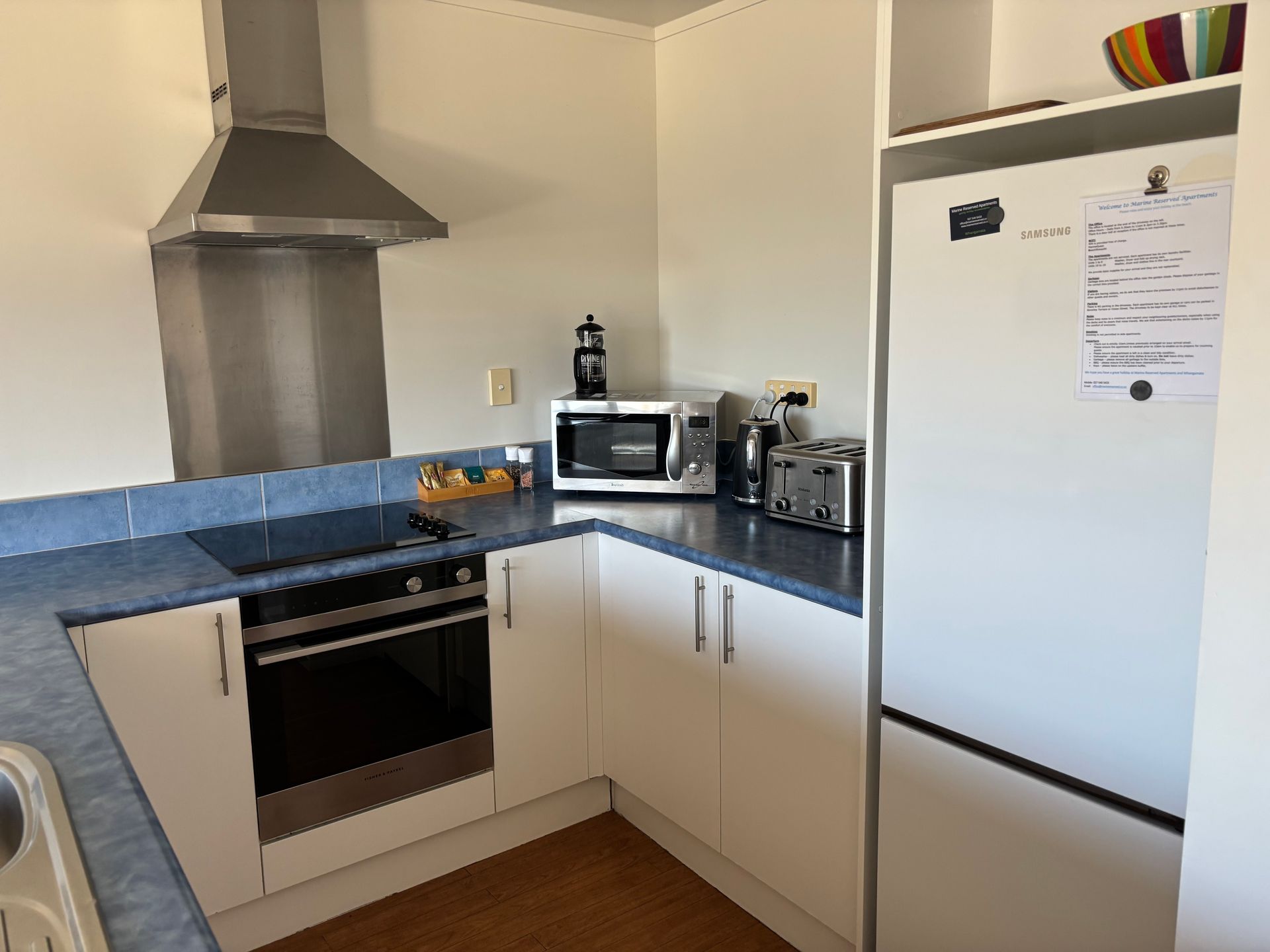Small white kitchen with blue countertops, stainless oven and hood, and a white refrigerator.