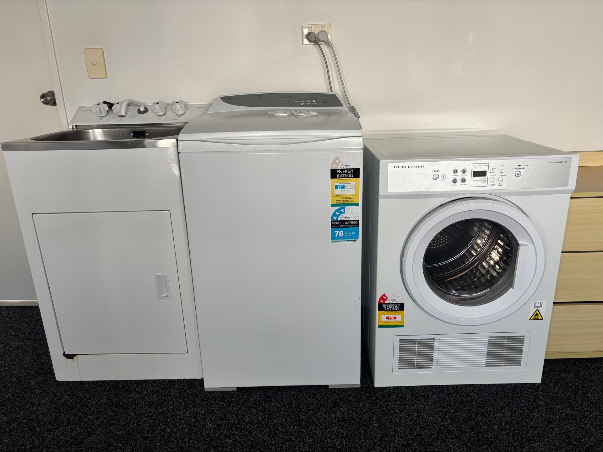 White dryer, top-load washer, and front-load washer lined up against a wall in a laundry room.