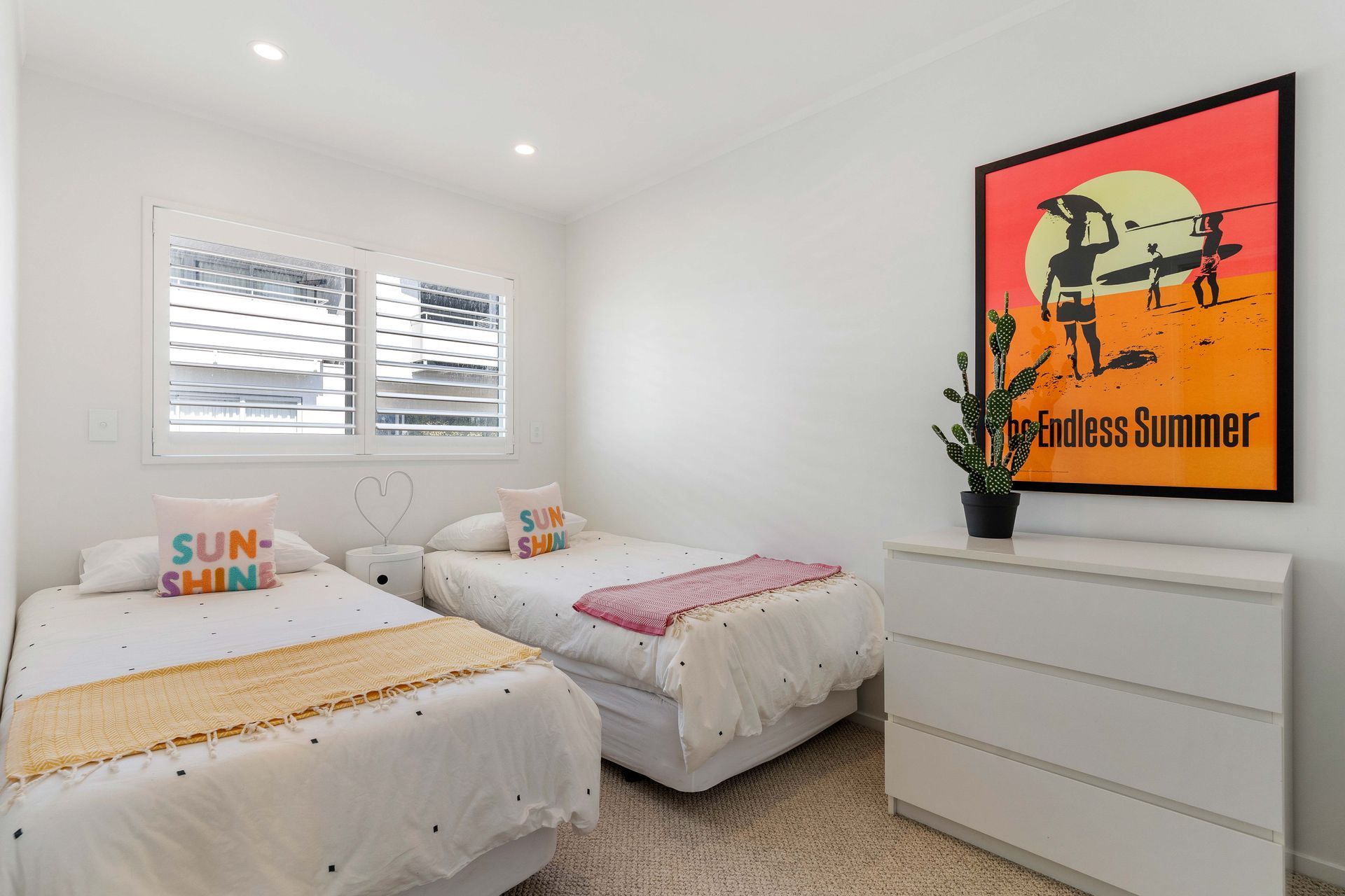 Bedroom with two twin beds, white walls, shuttered window. A 