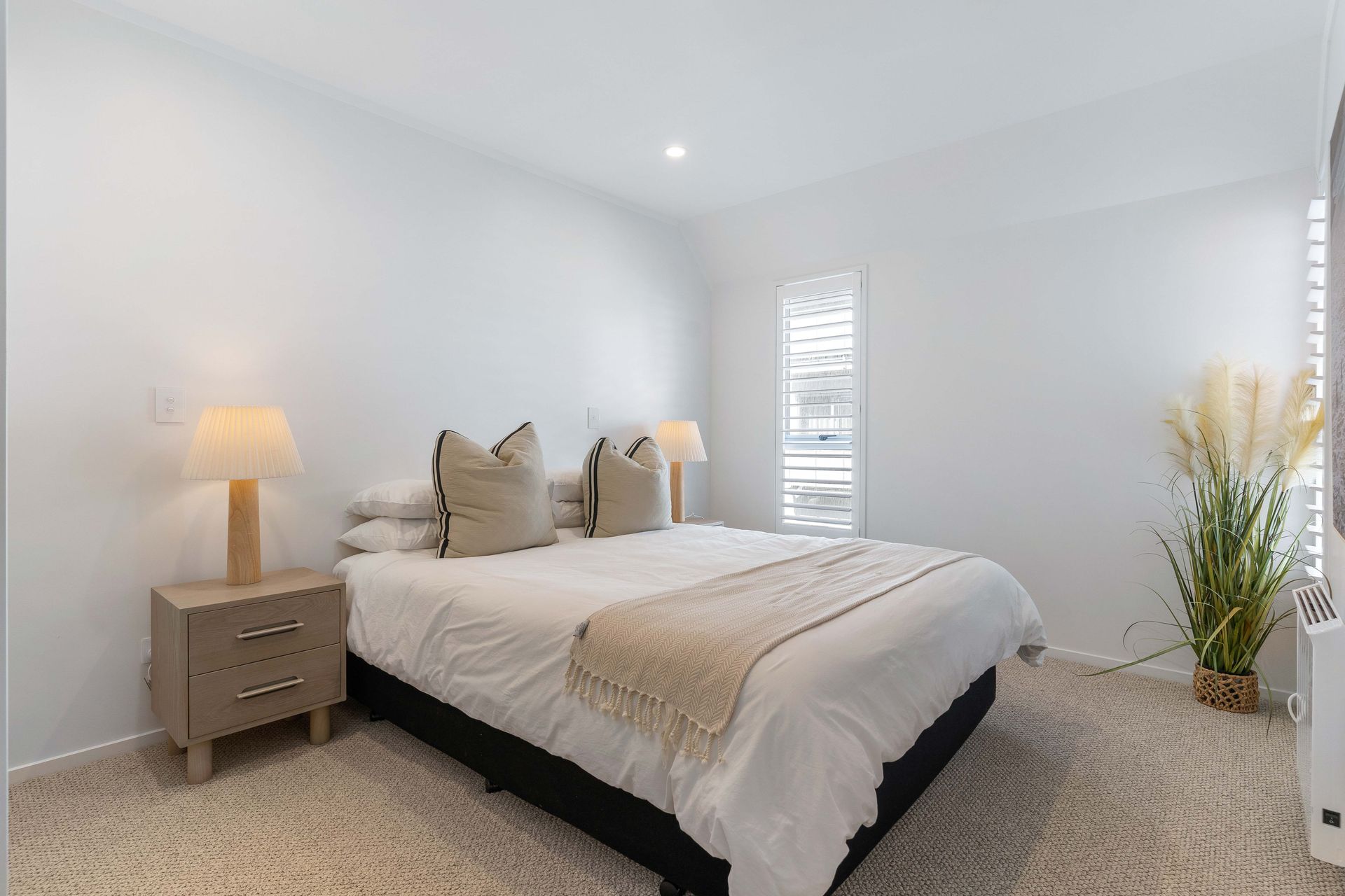 Bedroom with bed, nightstands, lamps, window, and decorative pampas grass in a neutral color scheme.