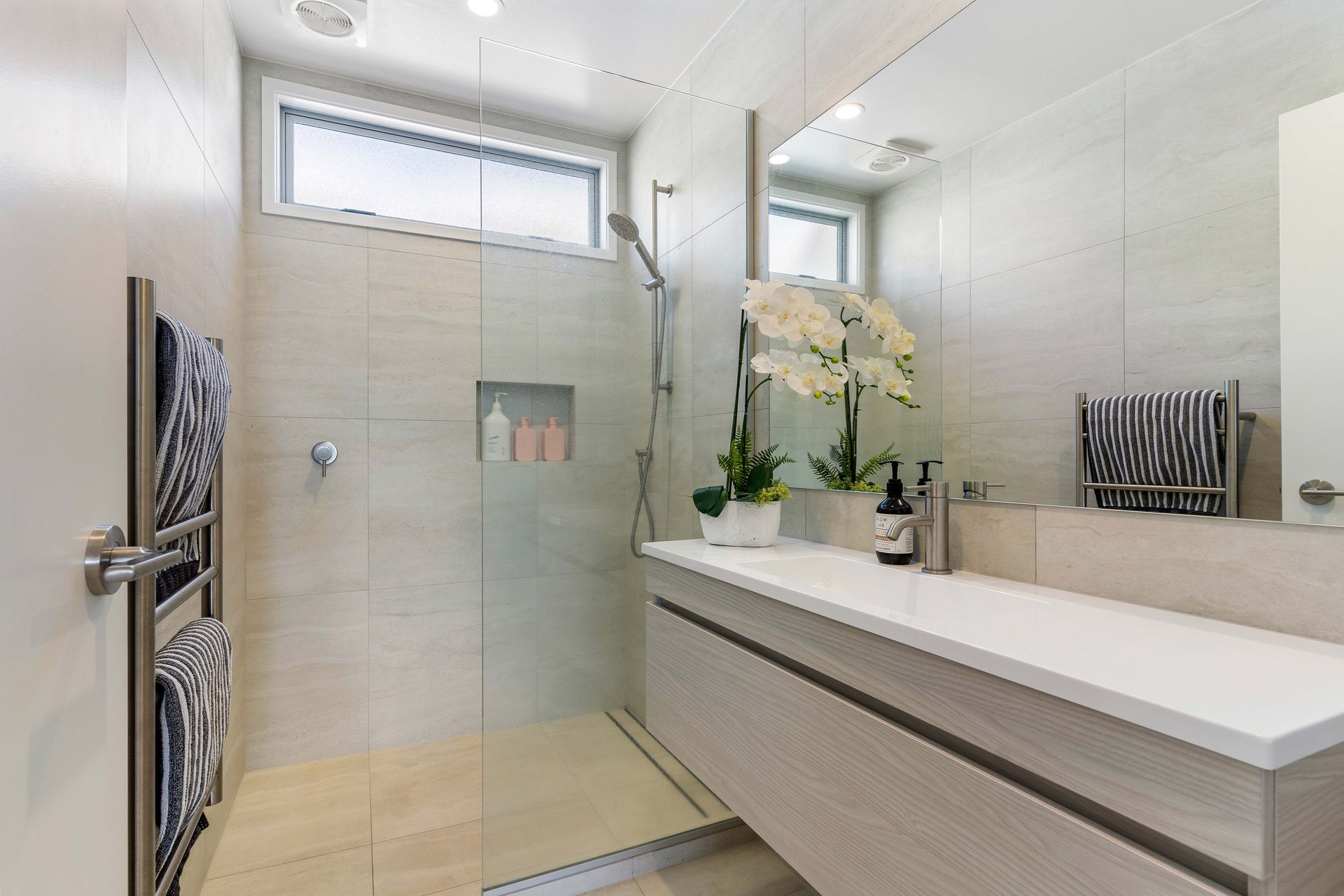 Modern bathroom with a shower, vanity, and neutral-colored tiles.