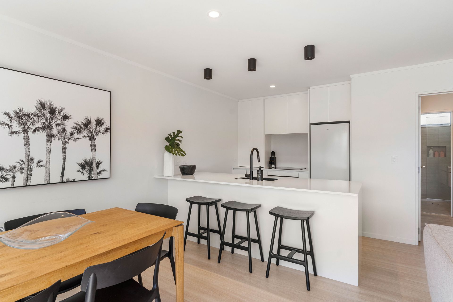 Modern kitchen and dining area with white cabinets, wood table, and black stools.